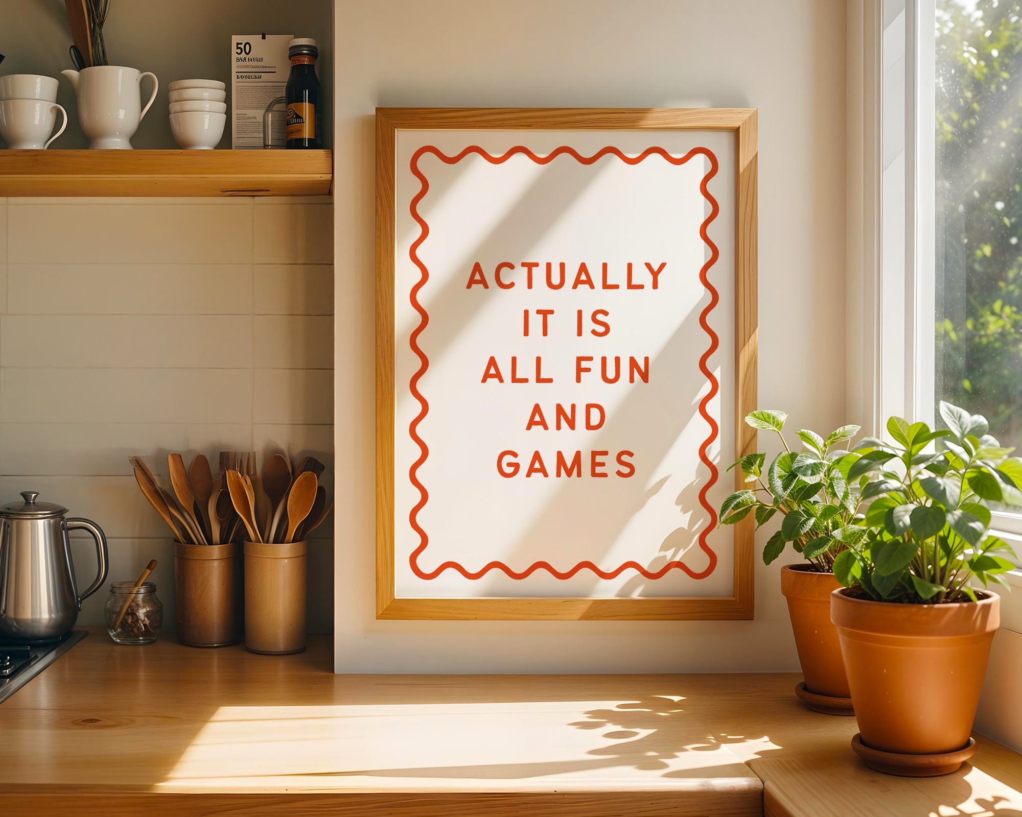 Framed poster with 'Actually it is all fun and games' text in a kitchen setting with plants and shelves.