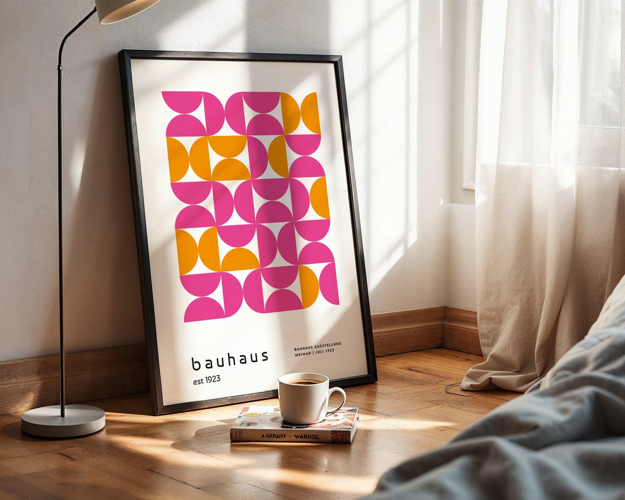 Framed Bauhaus poster on a wall with a cup and book on a wooden floor.
