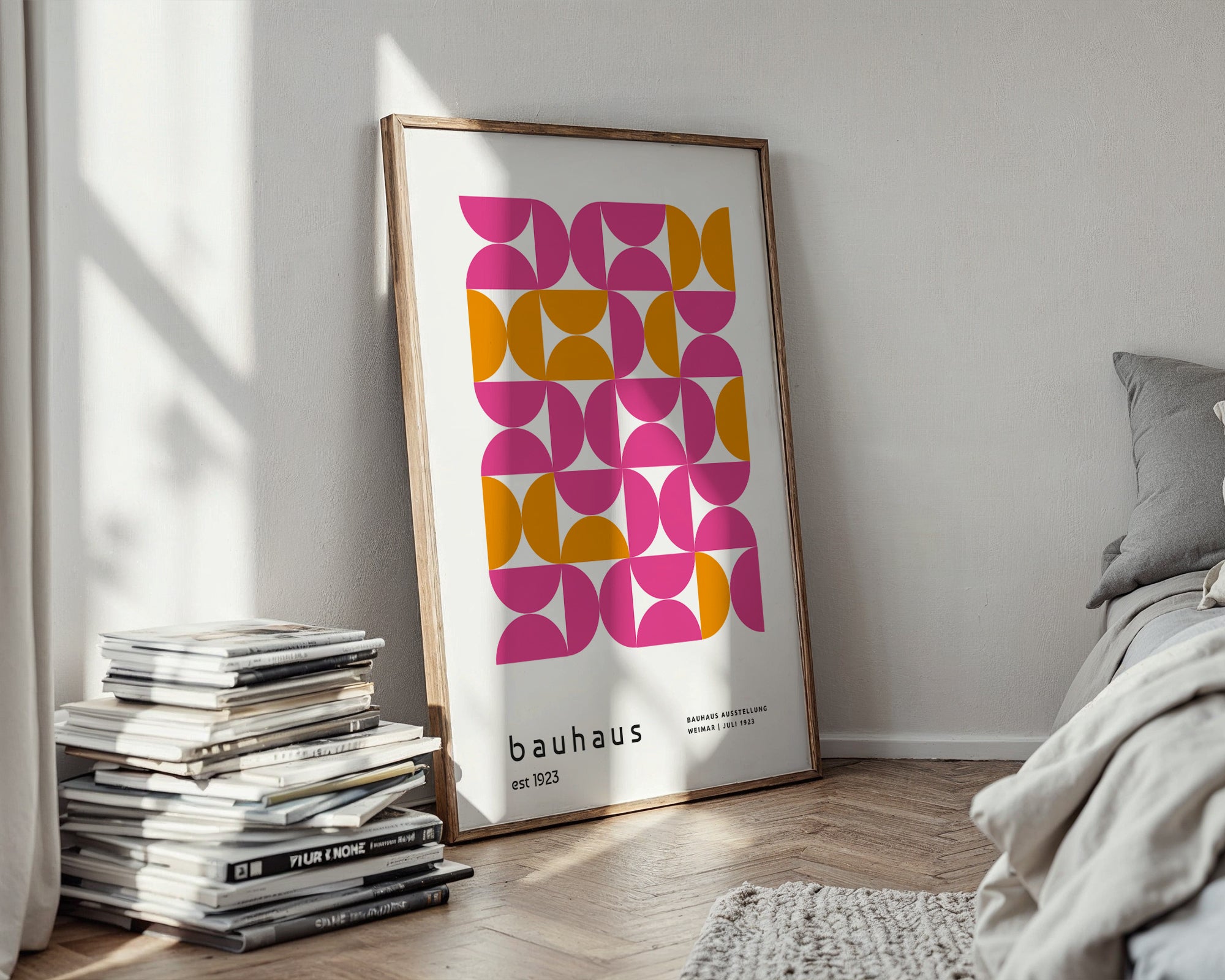 Framed Bauhaus poster on a wall with books and a bed in the background