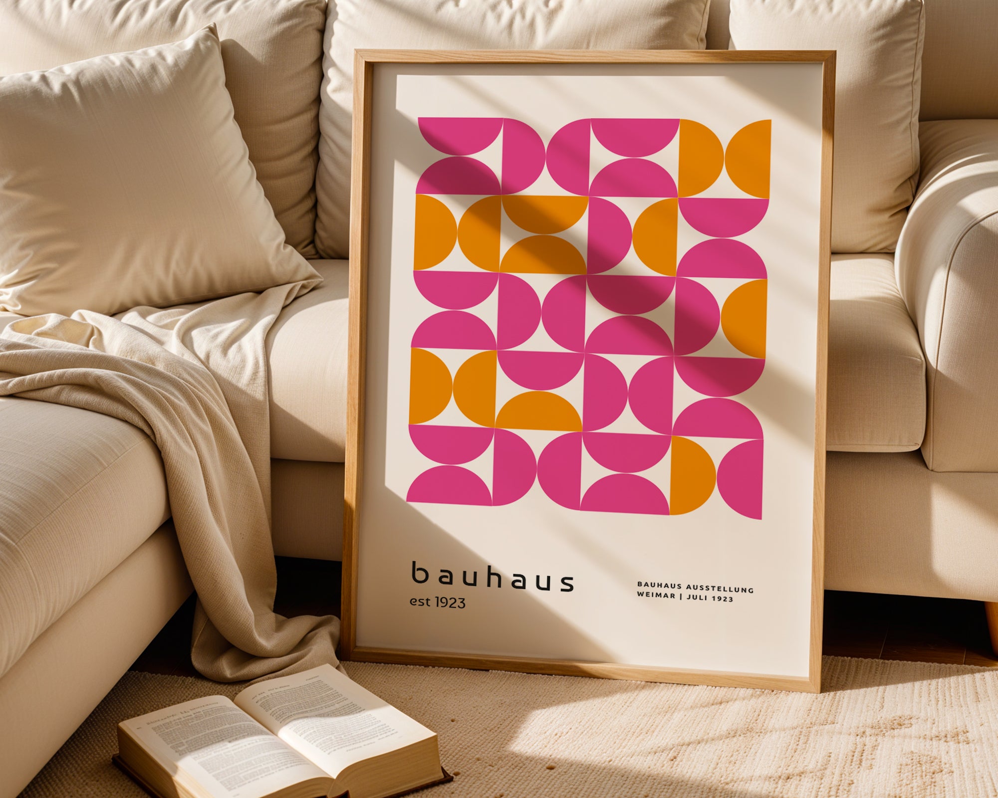 Framed Bauhaus-style poster on a beige couch with an open book.