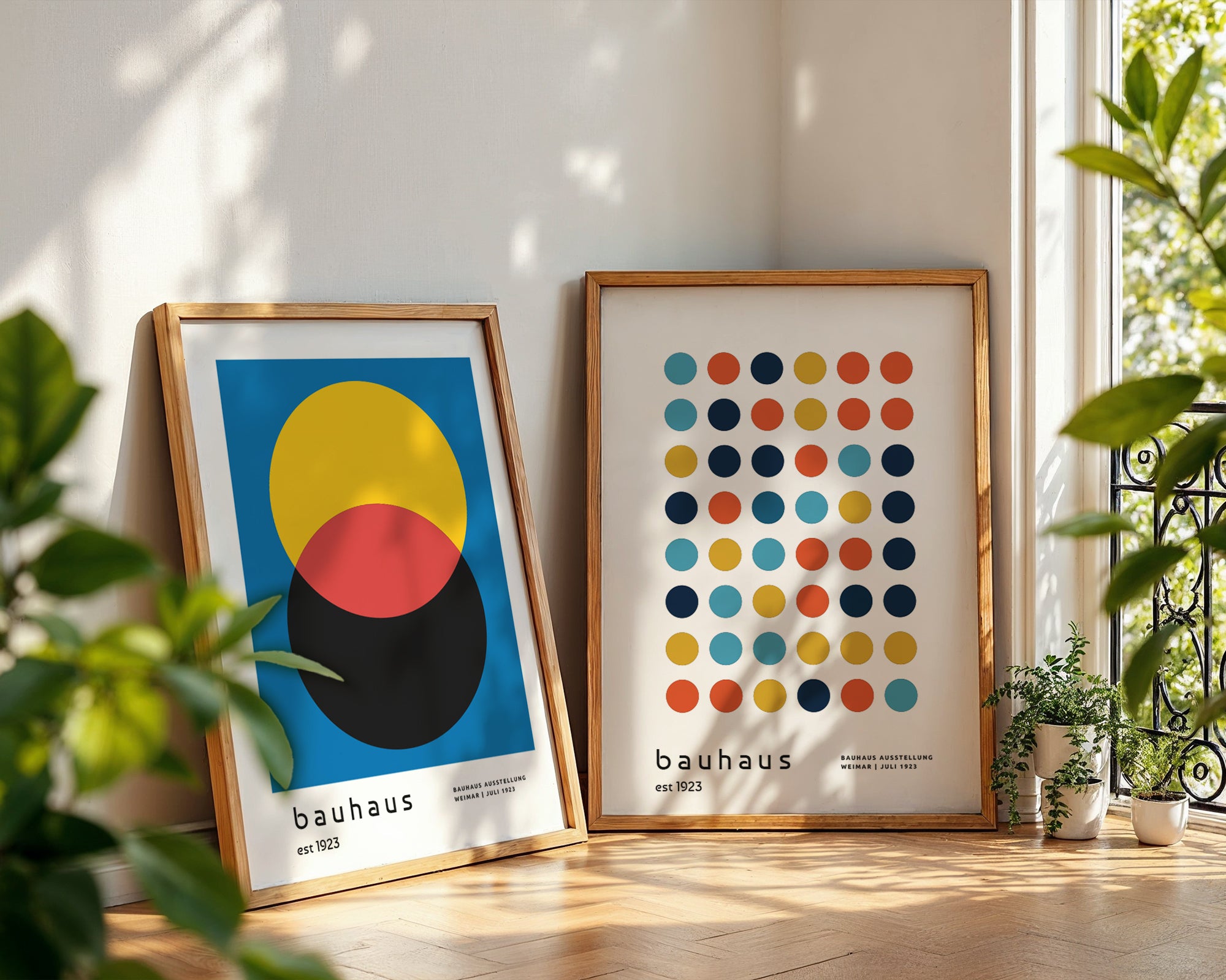 Two framed Bauhaus posters on a light wooden floor with plants around.