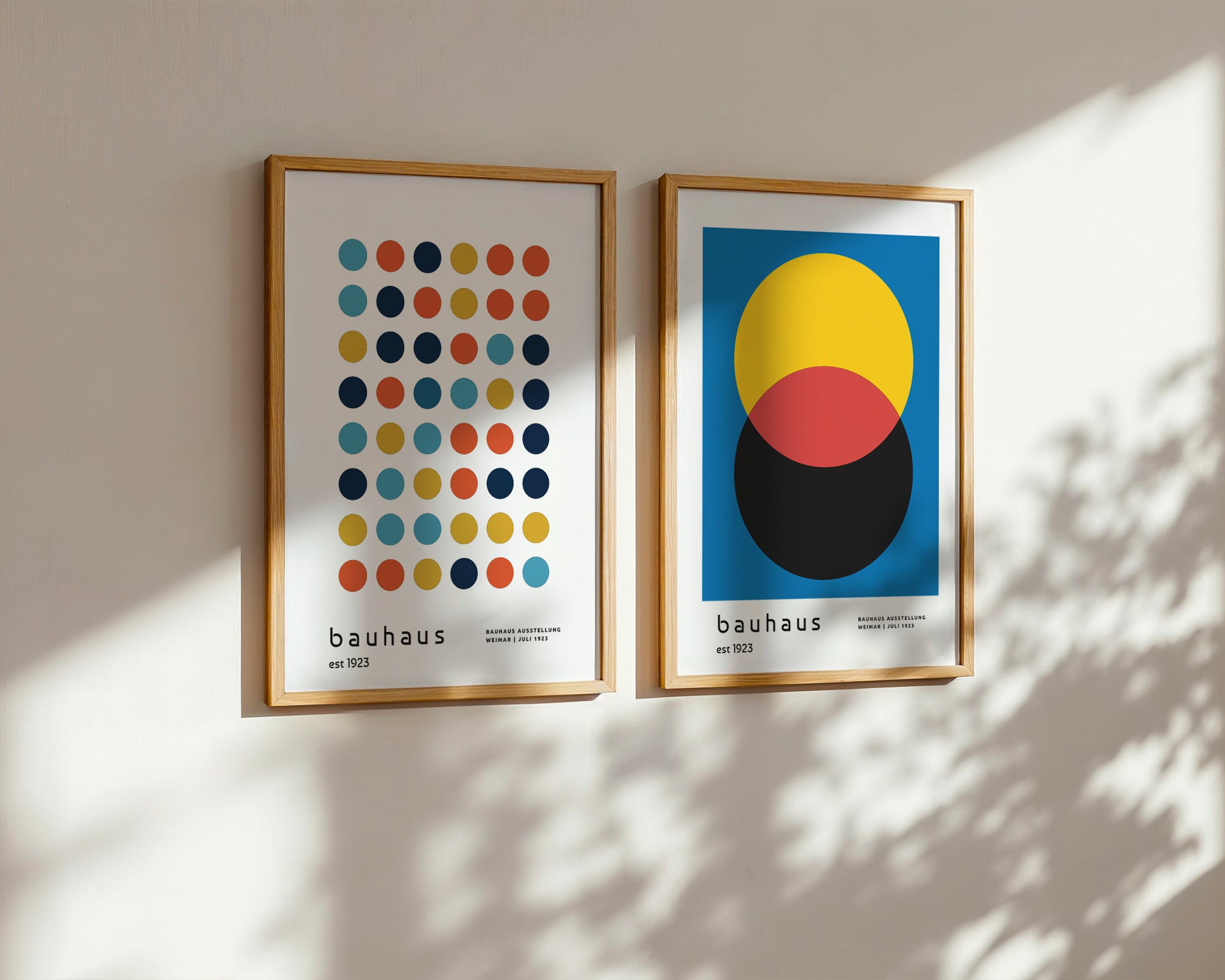 Two framed Bauhaus art prints on a wall with sunlight casting shadows.