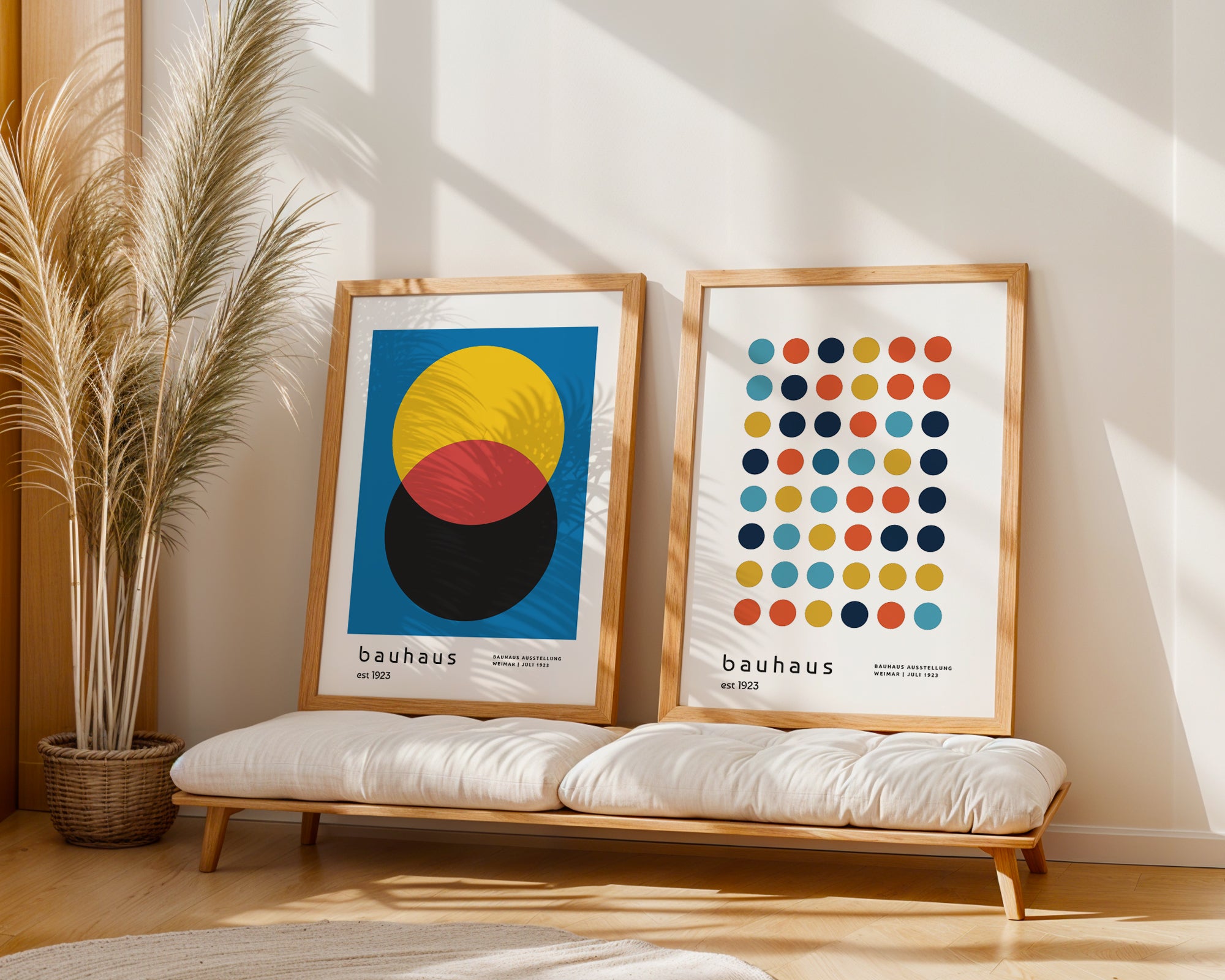 Two framed Bauhaus posters on a bench with a plant in the background