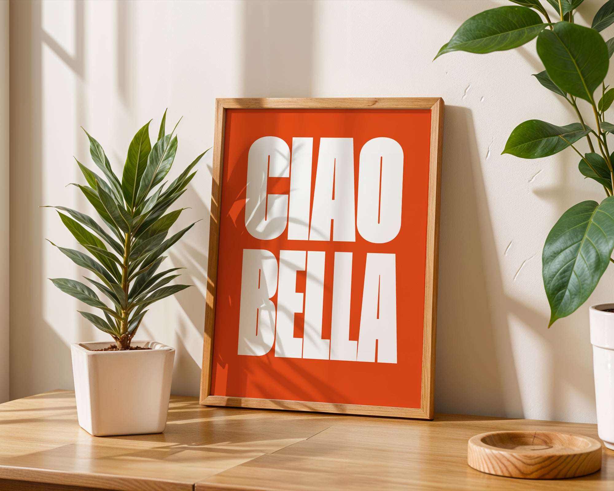 Framed artwork with 'CIAO BELLA' on a wooden table with plants