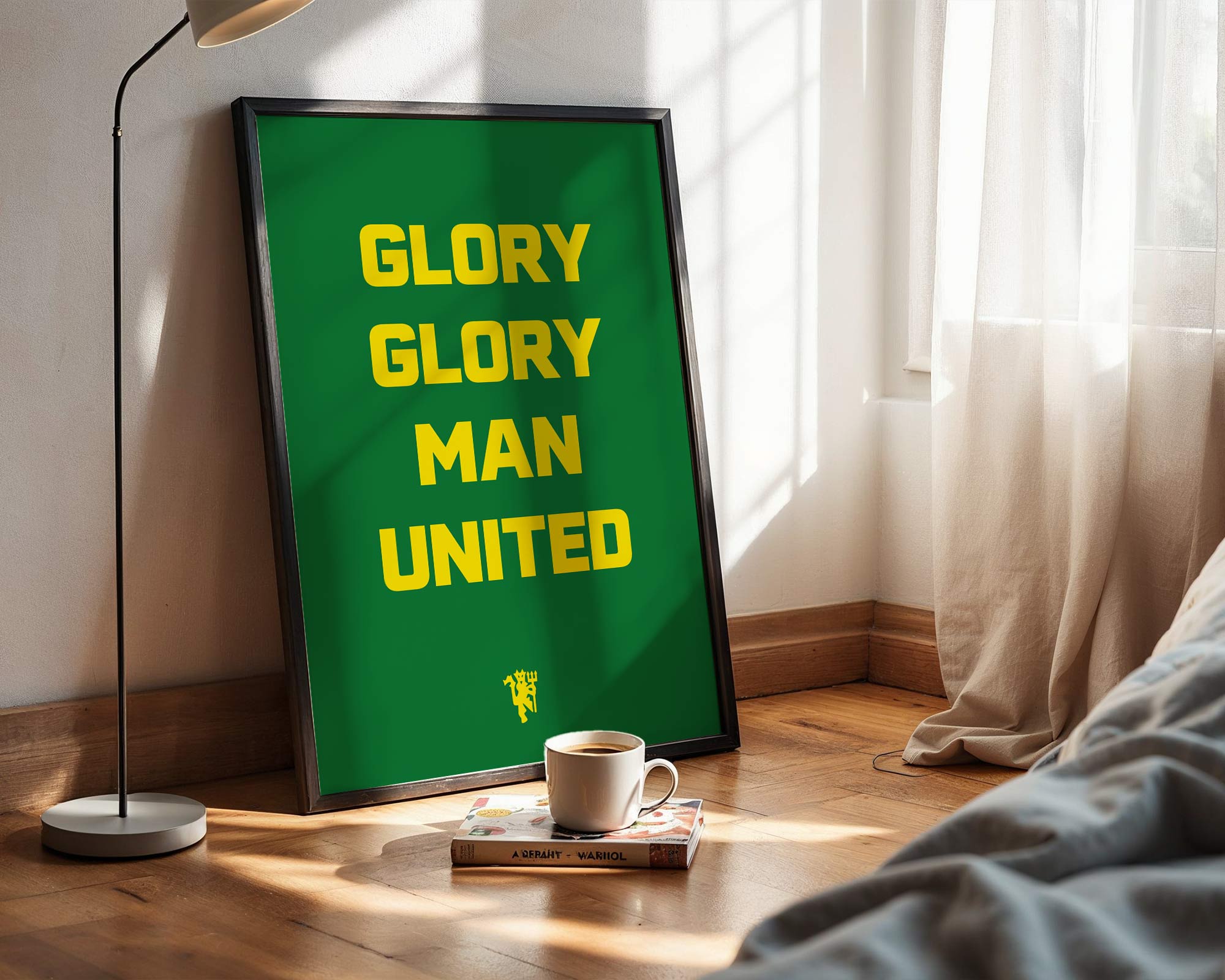 Framed poster with 'GLORY GLORY MAN UNITED' text in a room with a lamp and book on a wooden floor.