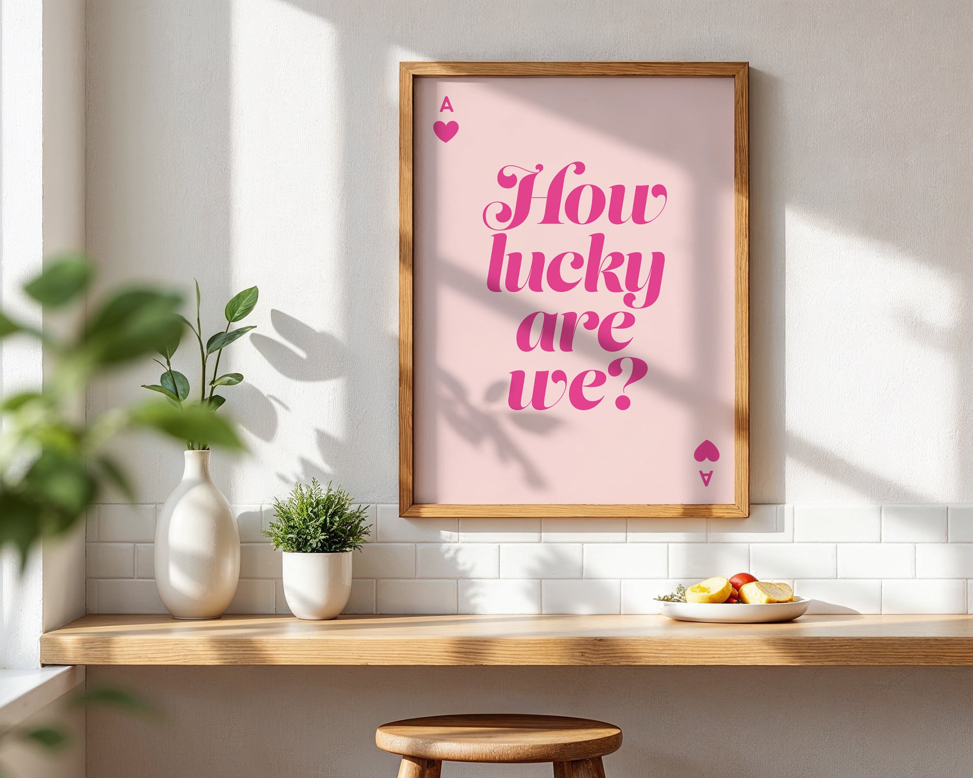 Framed poster with 'How lucky are we?' text on a wall with a table and plants below.