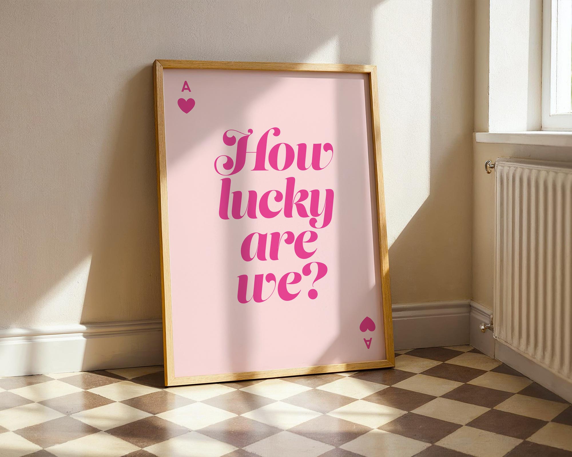 Framed poster with 'How lucky are we?' text on a pink background in a room with sunlight.