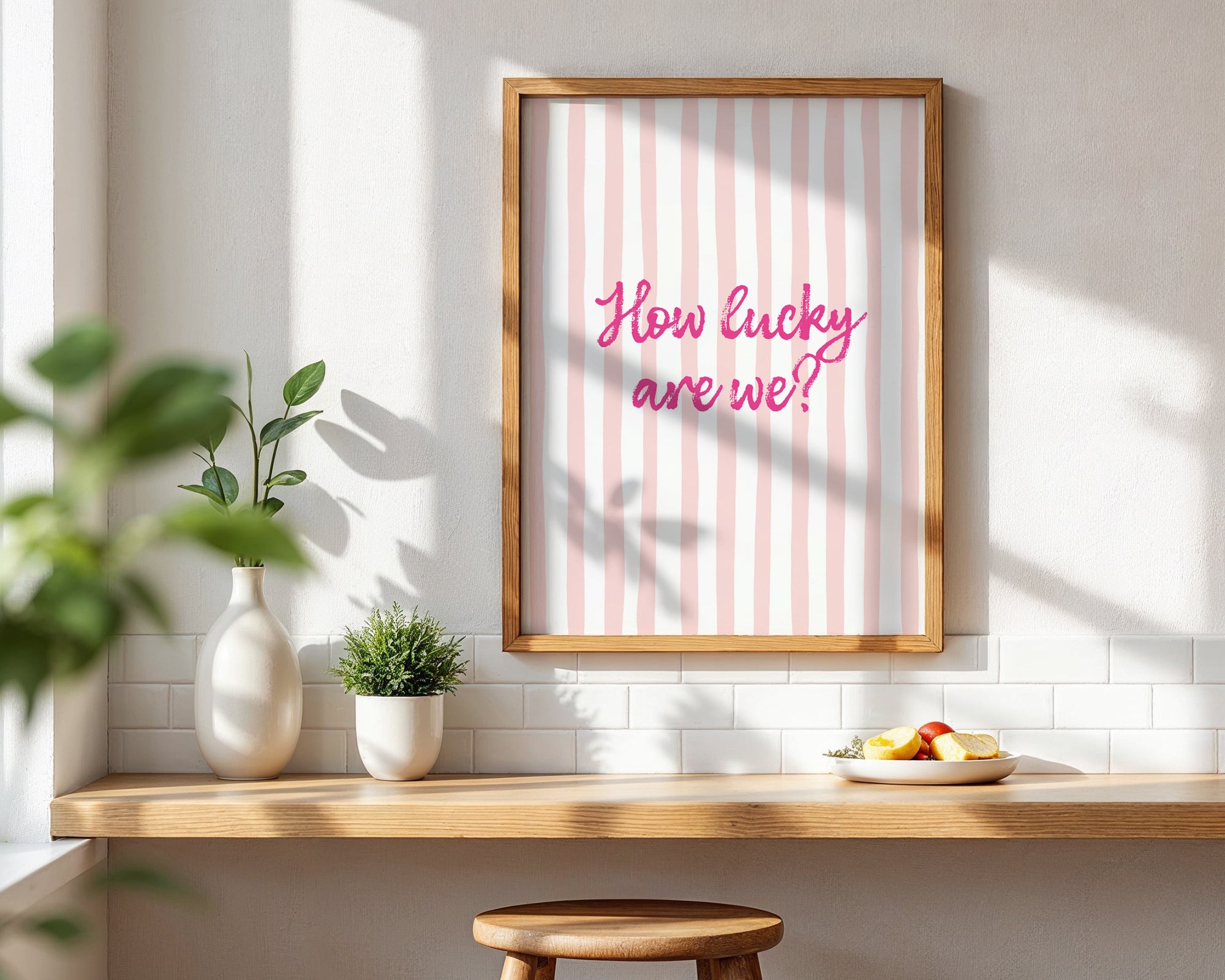 Framed print with 'How lucky are we?' text on a wall with a wooden shelf and plants.