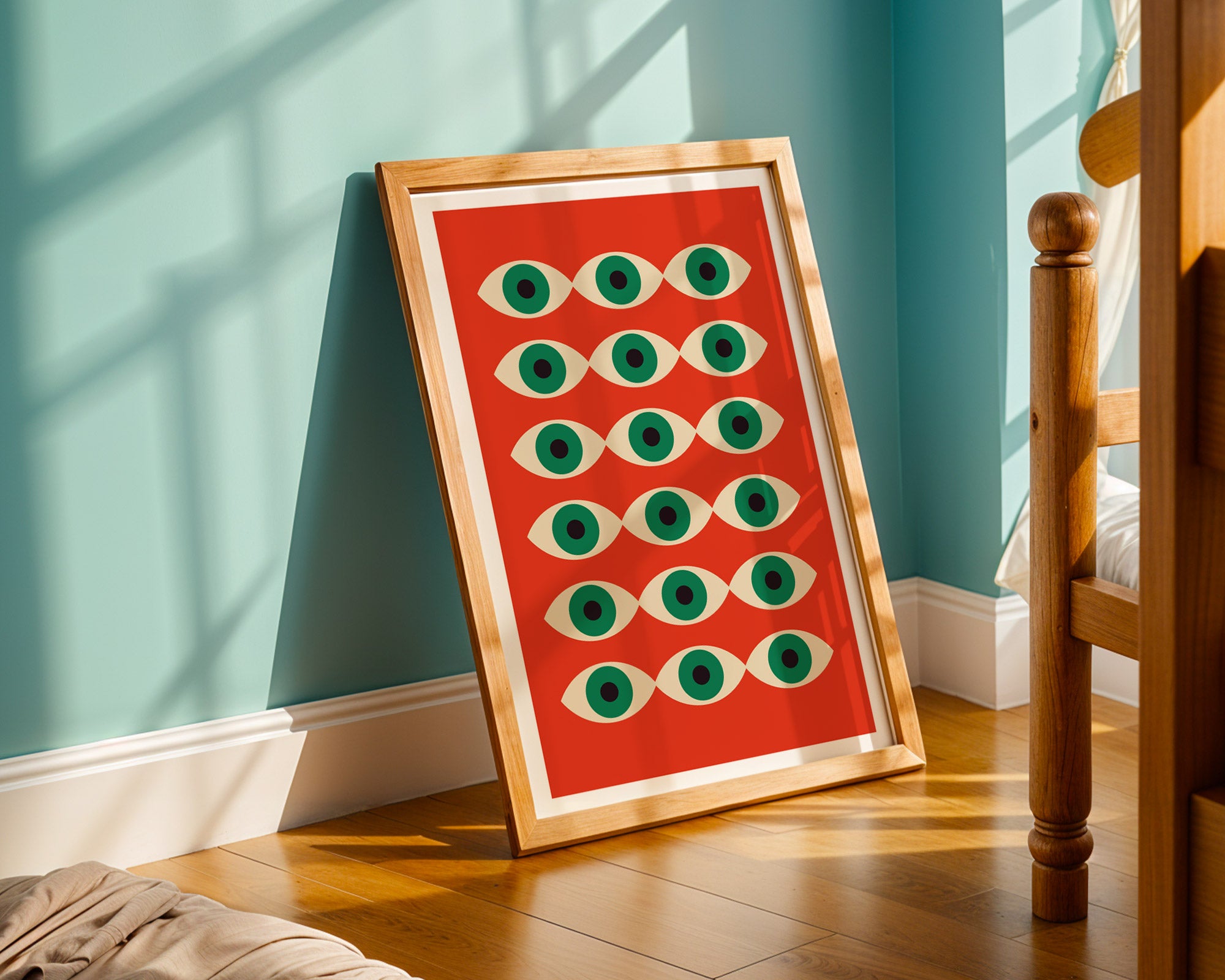 Framed artwork with green eyes on a red background in a room with wooden floor and teal wall.