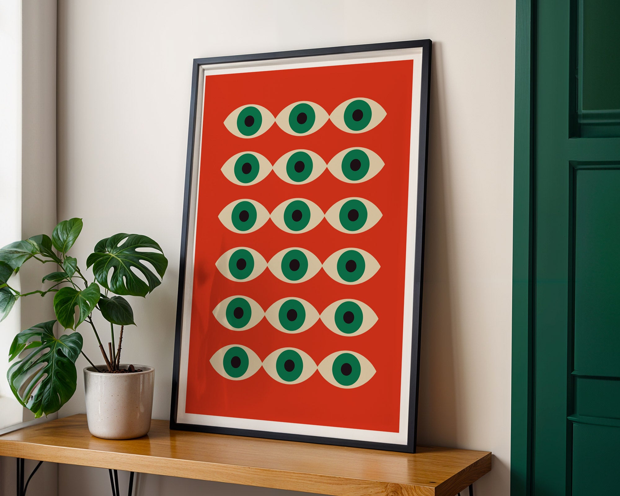 Framed abstract art print with green and white shapes on a red background, placed on a wooden shelf.