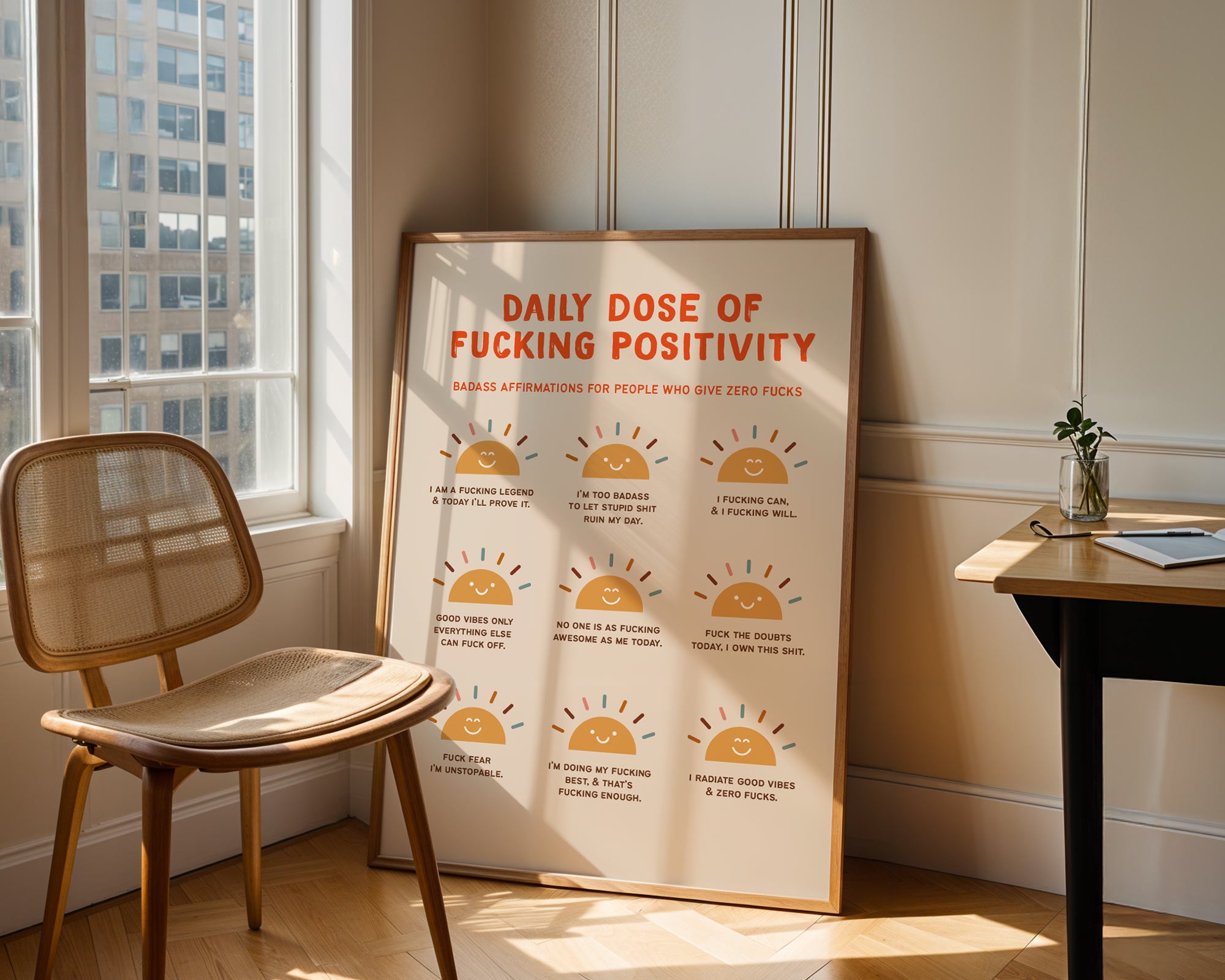 Framed poster with 'Daily Dose of Fucking Positivity' text in a room with a chair and window.