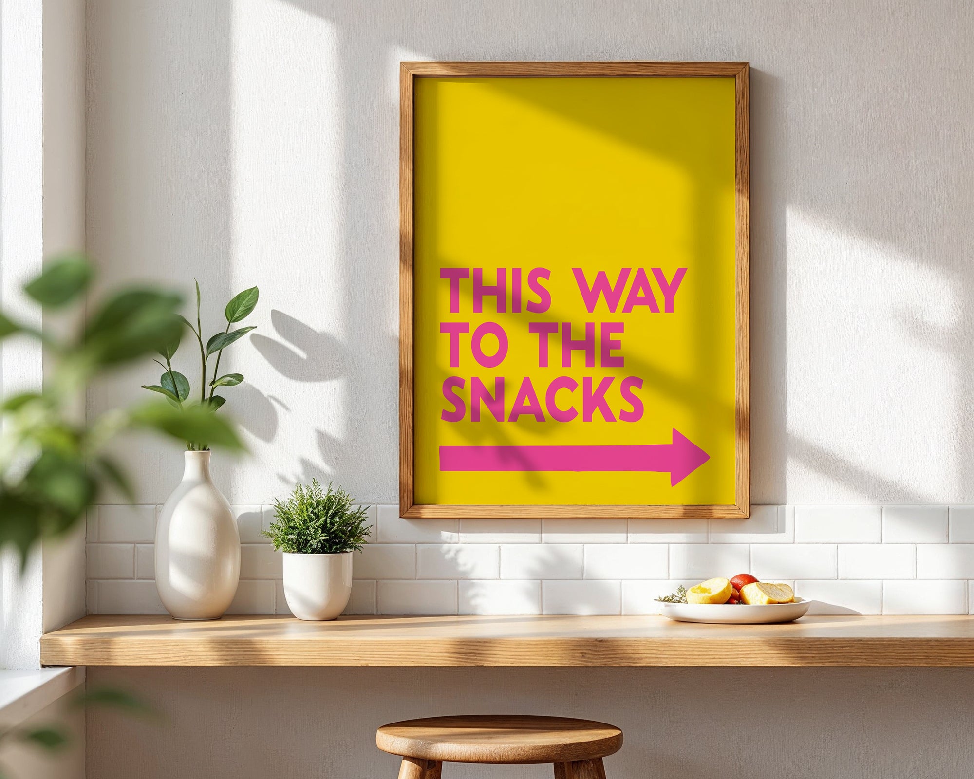 Yellow framed sign with pink text and arrow on a wall above a kitchen counter.