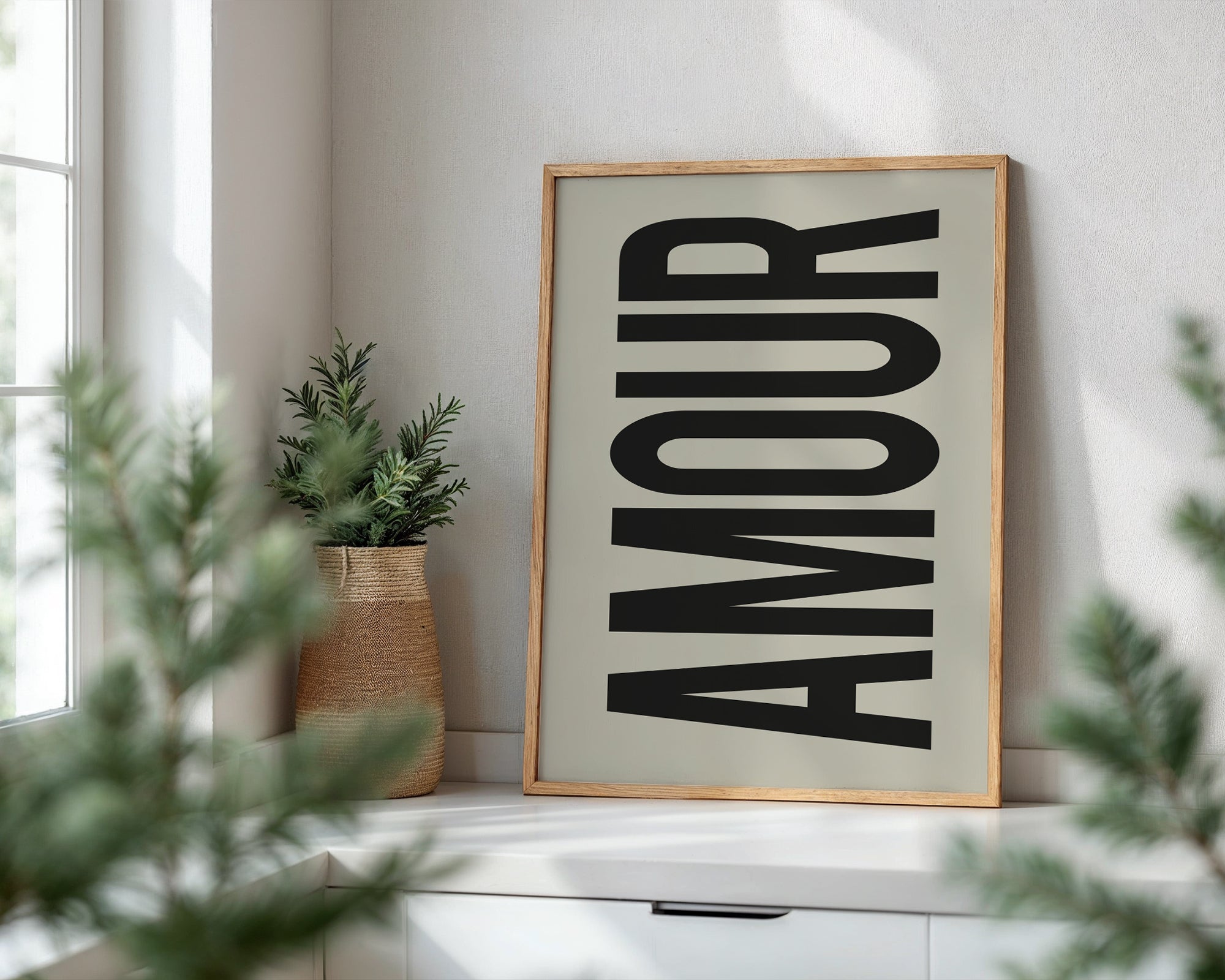 Framed artwork with the word 'AMOUR' on a white wall with plants around.