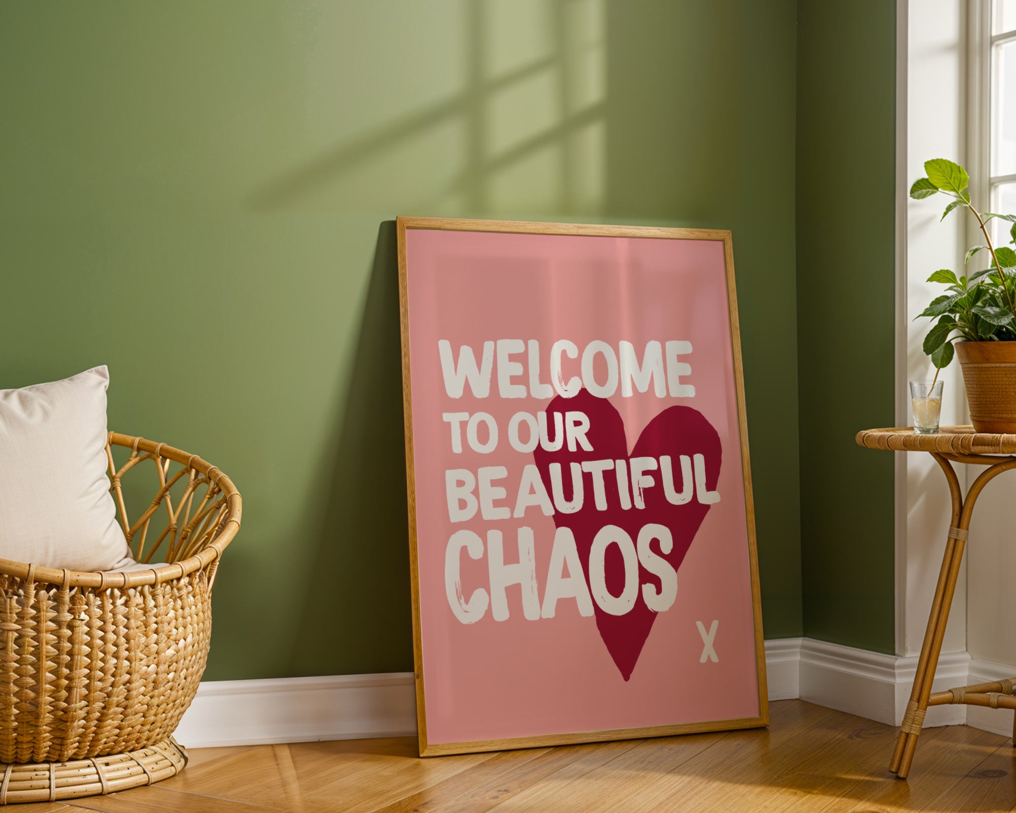 Pink framed poster with 'Welcome to our Beautiful Chaos' text in a room with green walls and wooden floor.