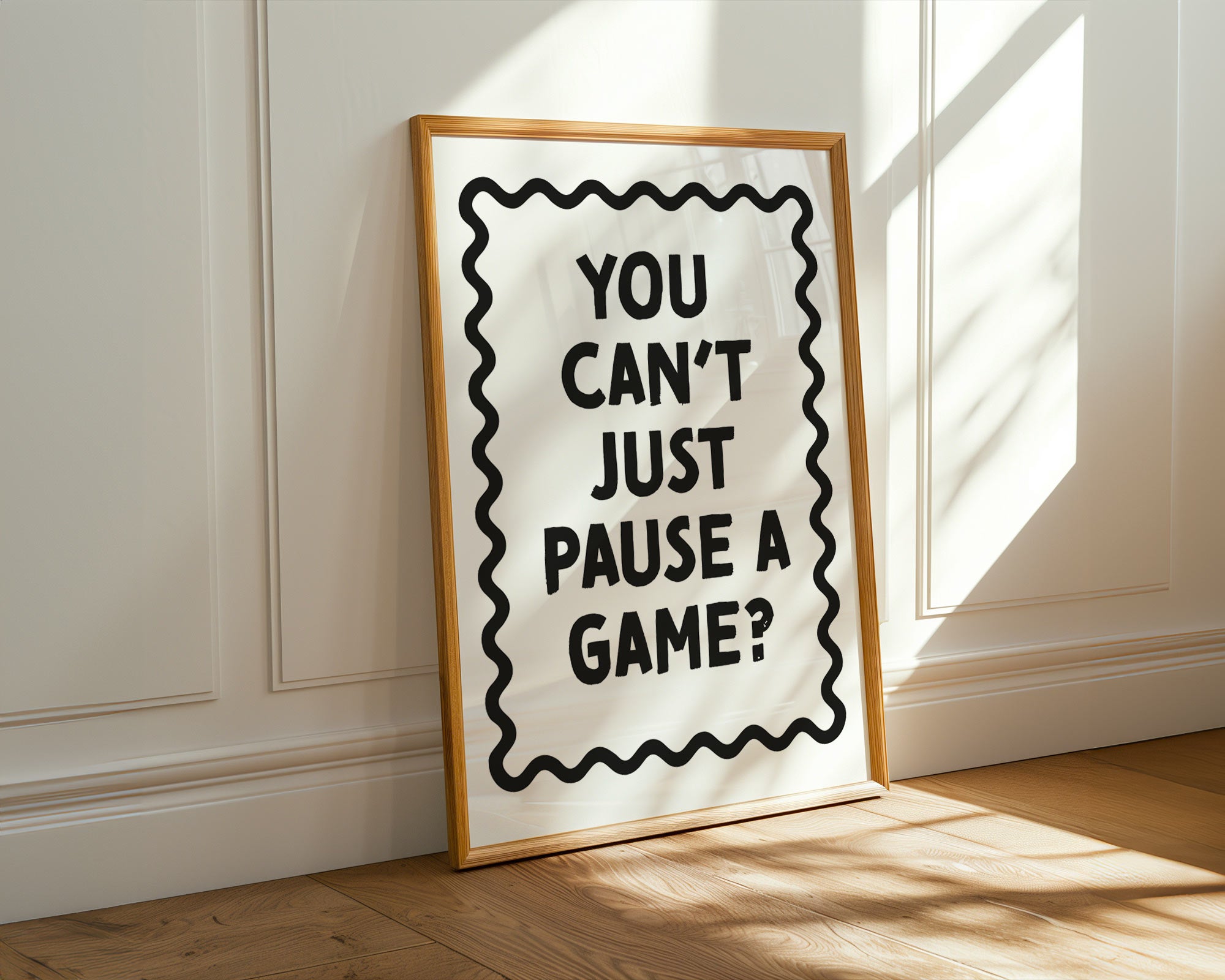 Framed poster with text 'YOU CAN'T JUST PAUSE A GAME?' on a wall.