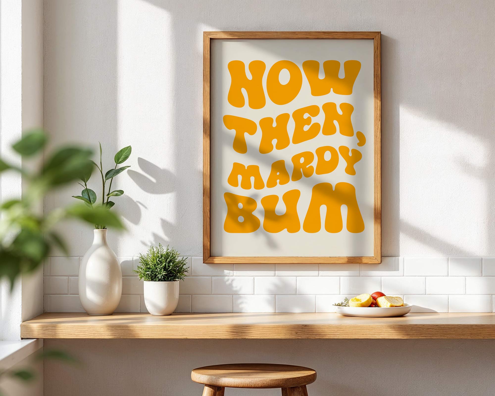 Framed artwork with humorous text on a wall in a room with a wooden shelf and plants.