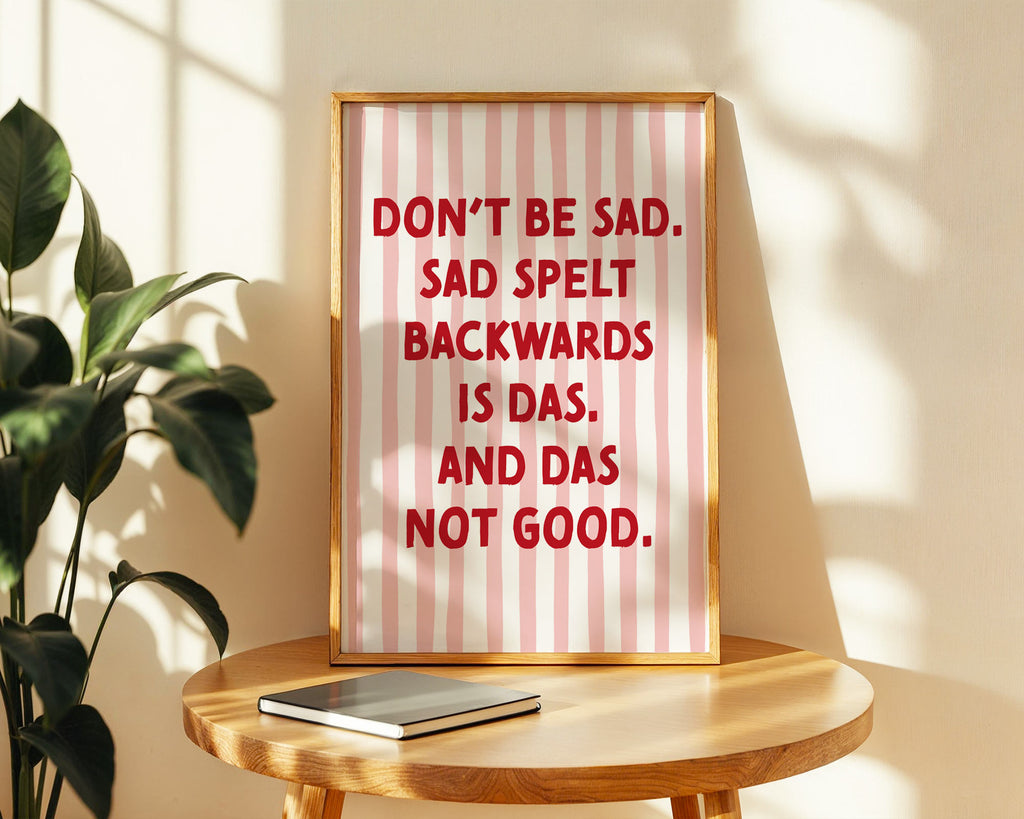 Framed poster with humorous text on a wooden table with a plant in the background