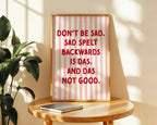 Framed poster with humorous text on a wooden table with a plant in the background