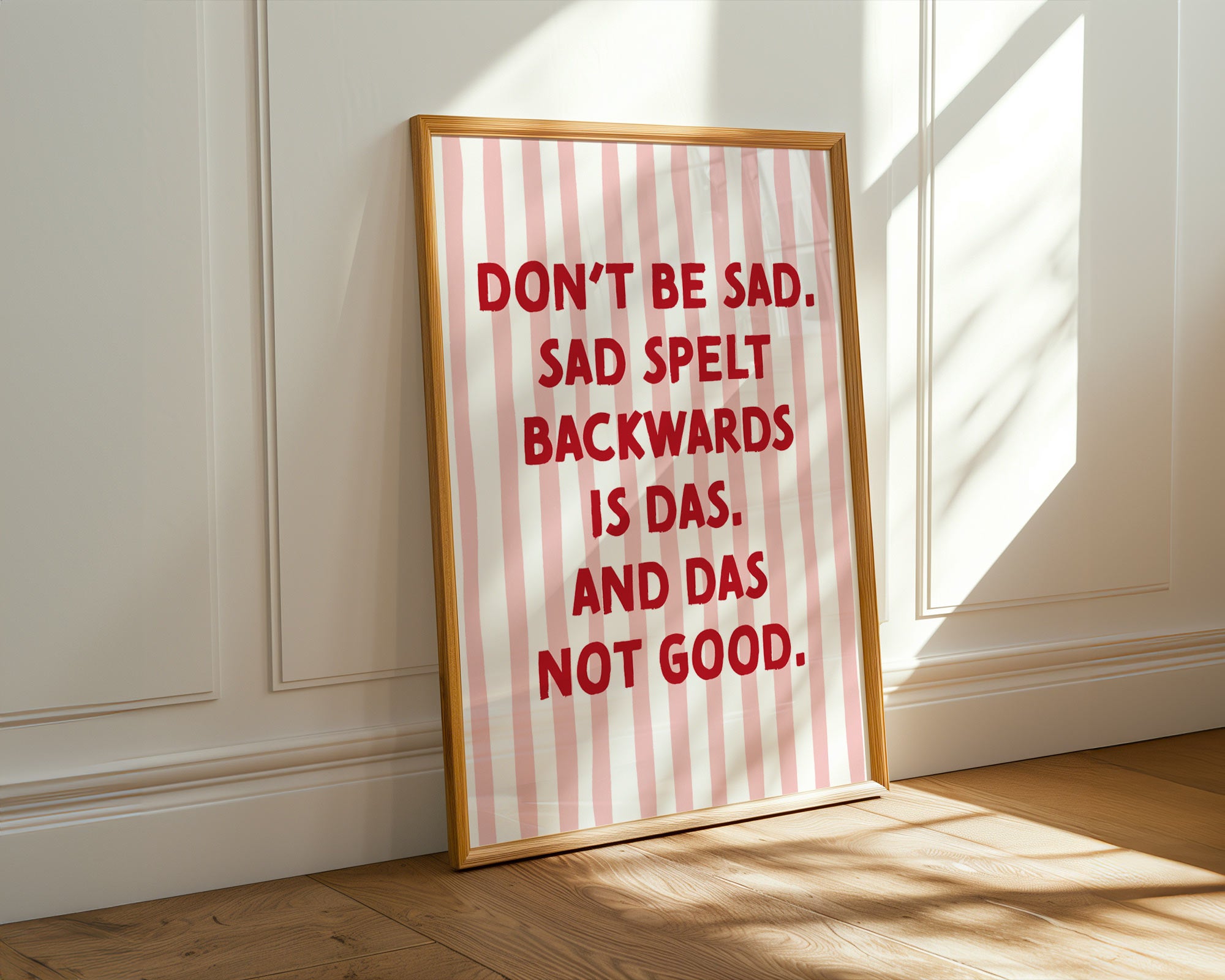 Framed poster with red text on a striped background, leaning against a white wall.