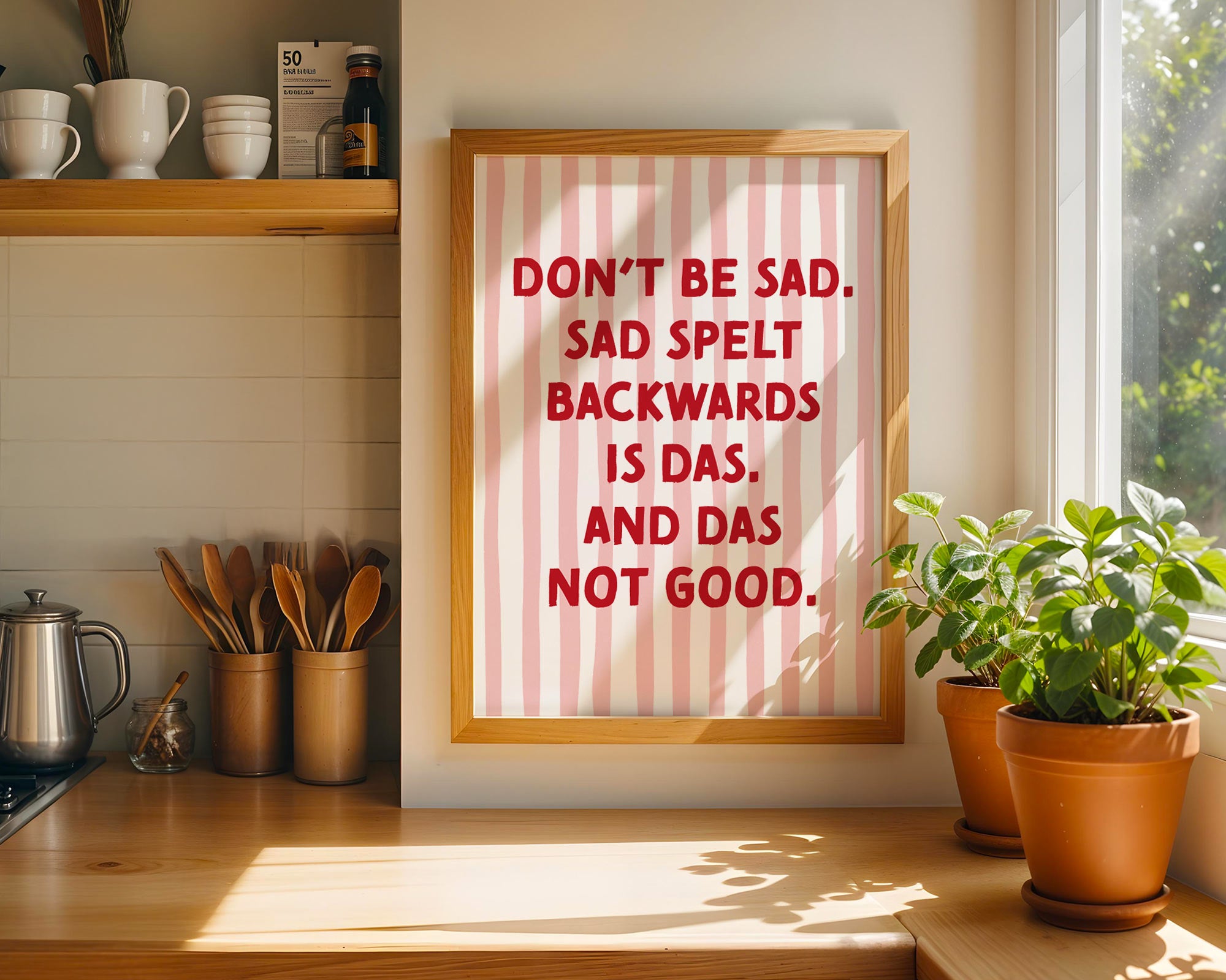 Framed humorous print on a kitchen wall with plants and kitchenware.