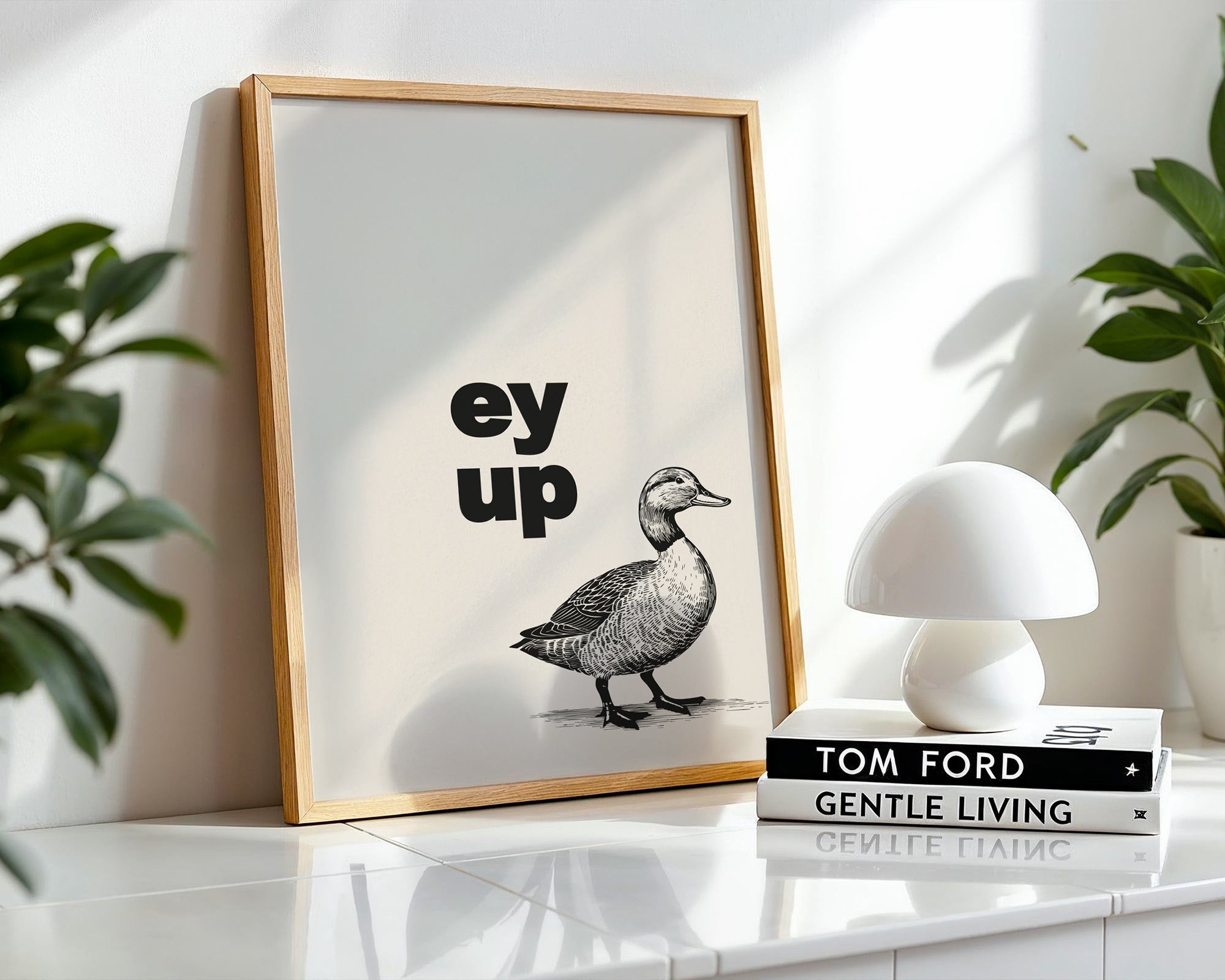 Framed artwork with a duck illustration and text on a shelf with books and a lamp.