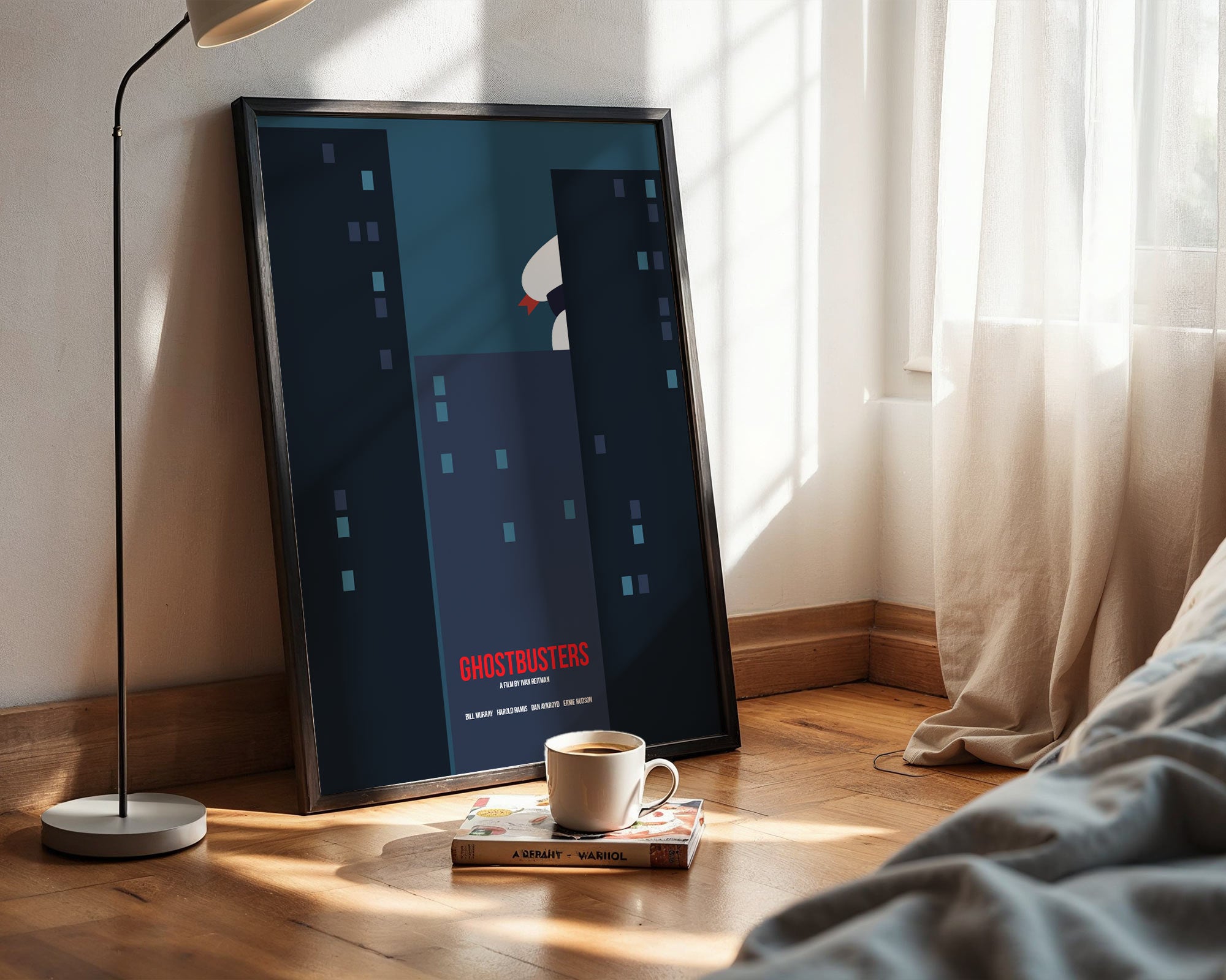 Framed poster of 'Ghostbusters' on a wall next to a bed with a lamp and cup.