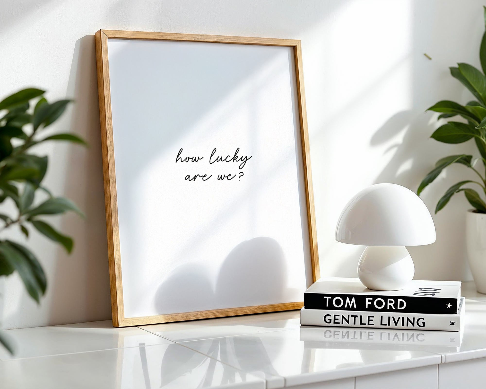 Framed print with 'how lucky are we?' text on a shelf with books and a lamp.