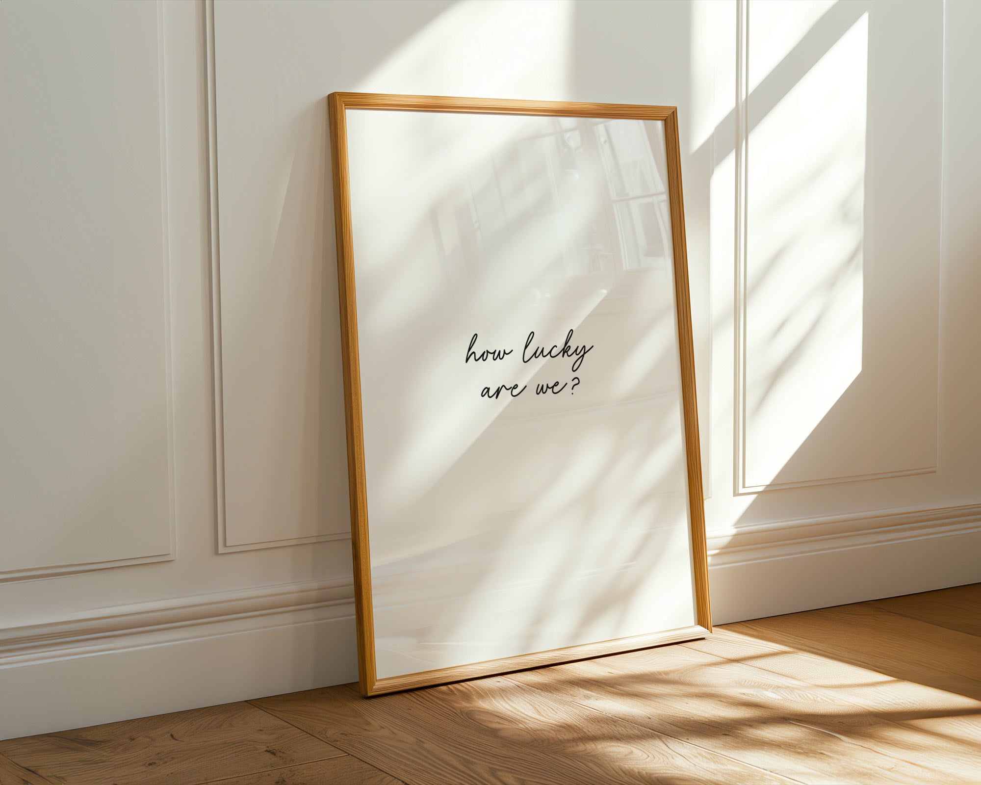 Framed print with 'how lucky are we?' text on a wall with sunlight casting shadows.