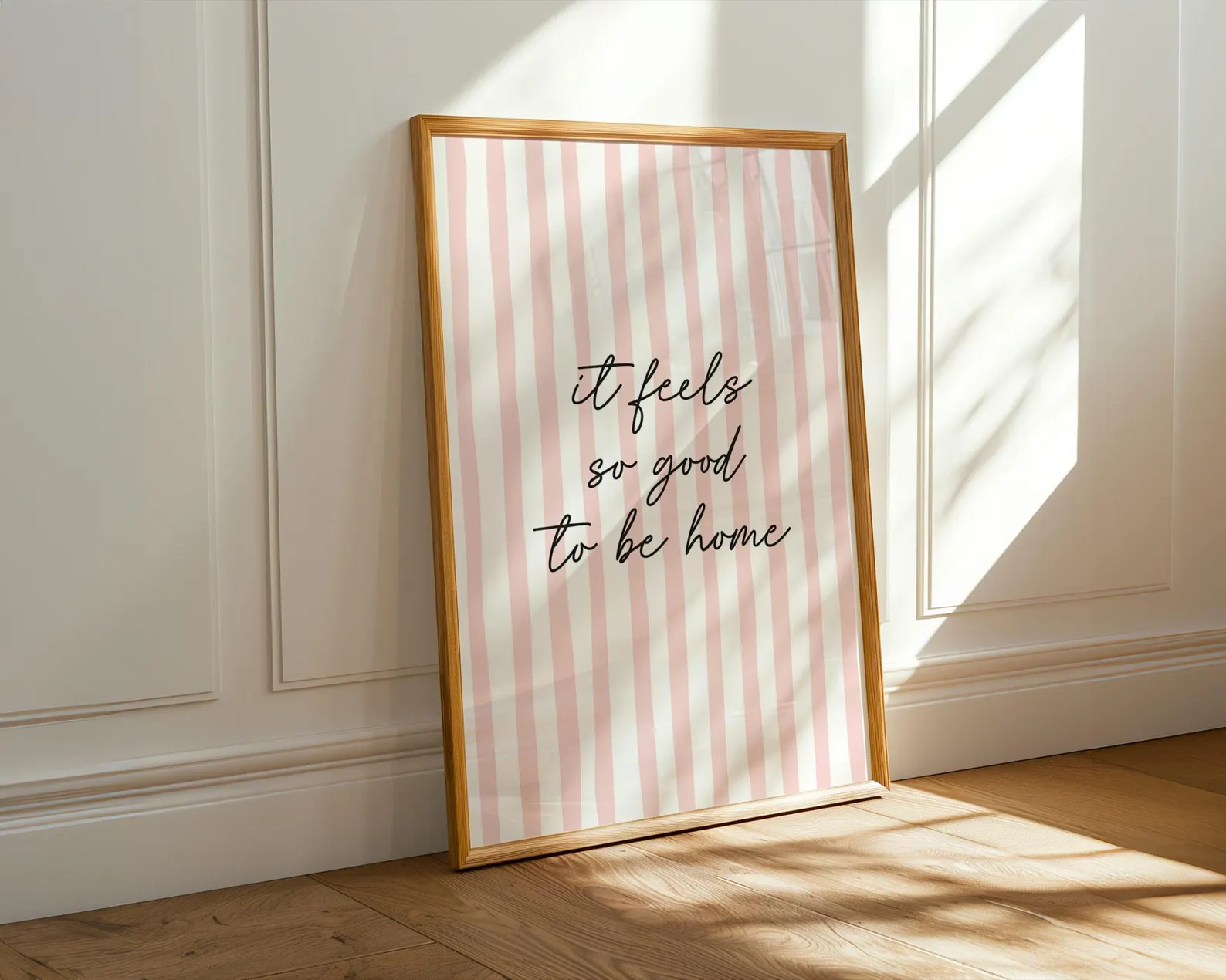 Framed print with 'it feels so good to be home' text on a striped background, placed against a wall.