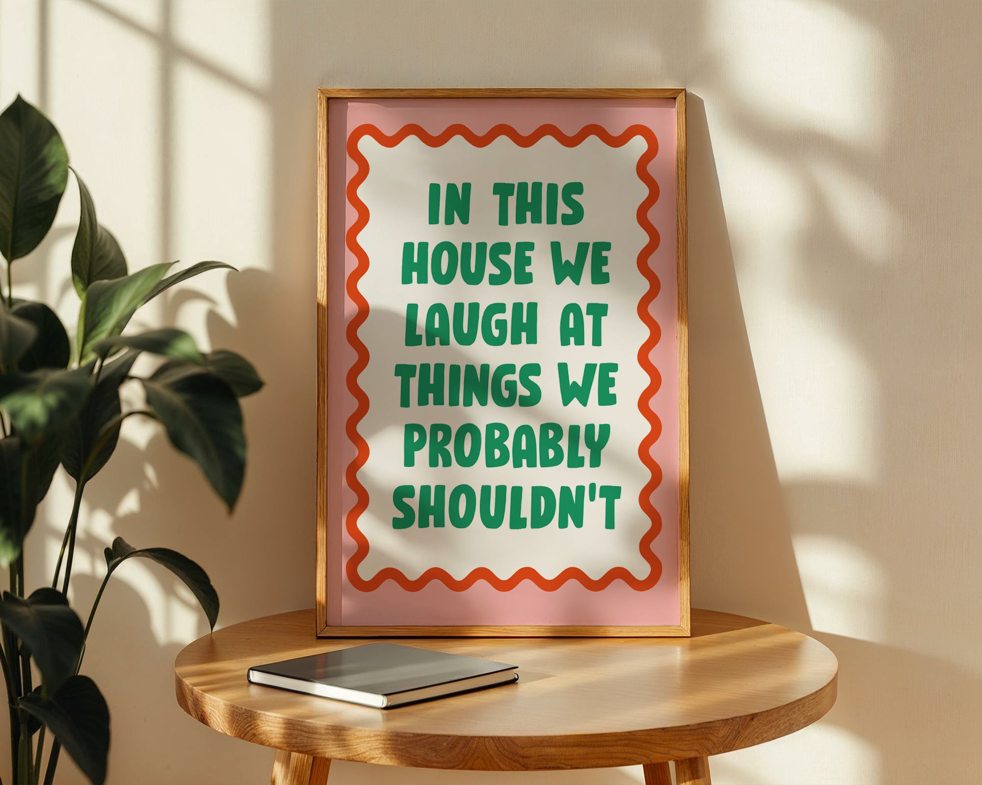 Framed sign with humorous quote on a wooden table with a plant in the background