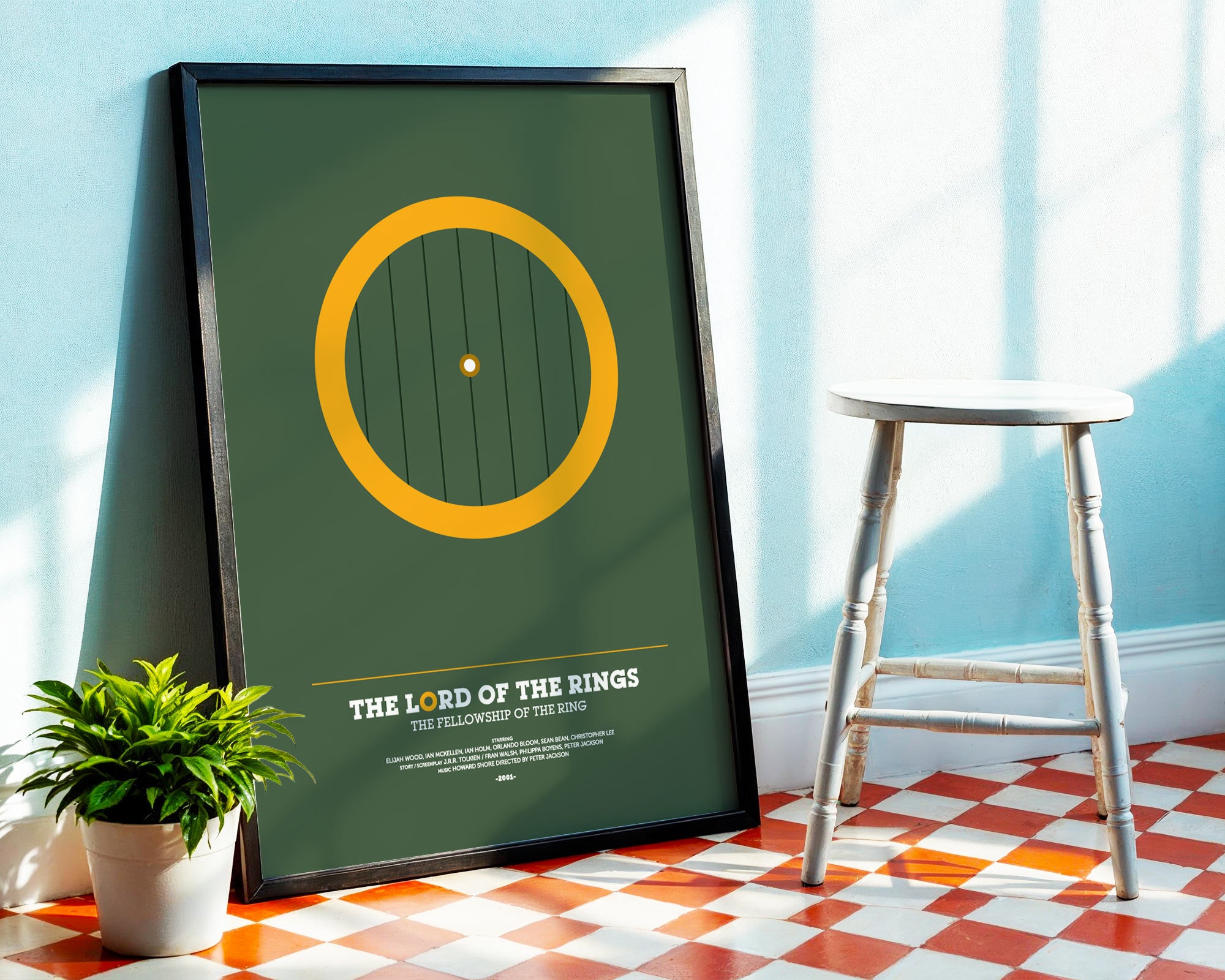 Framed poster of 'The Lord of the Rings' design on a wall with a stool and plant in the background.