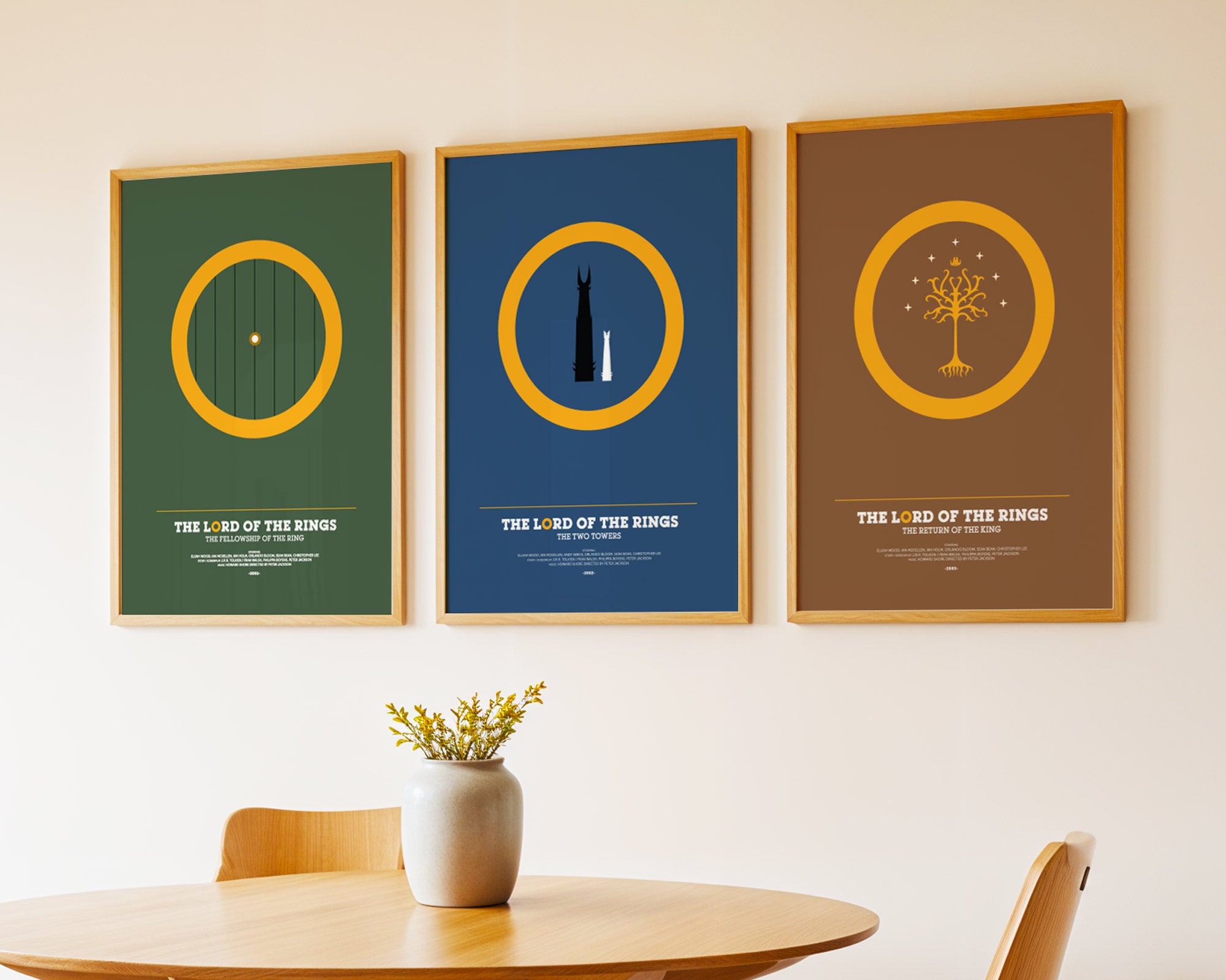 Three framed posters of 'The Lord of the Rings' series on a wall above a table.