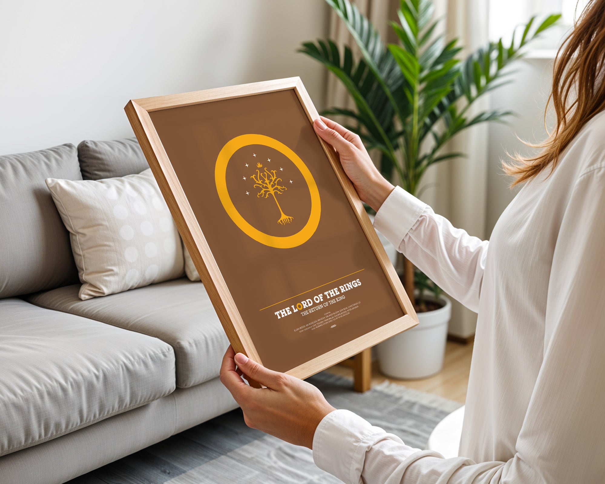 Person holding a framed poster with a design and text in a living room.