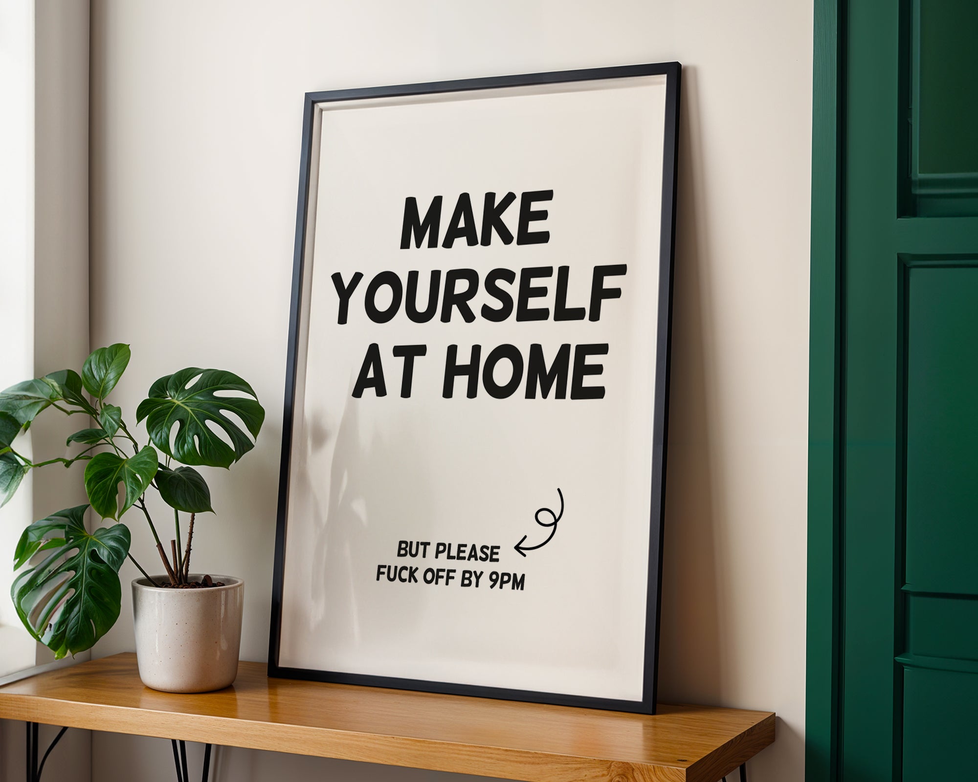Framed poster with text 'MAKE YOURSELF AT HOME BUT PLEASE FUCK OFF BY 9PM' on a wall next to a plant.