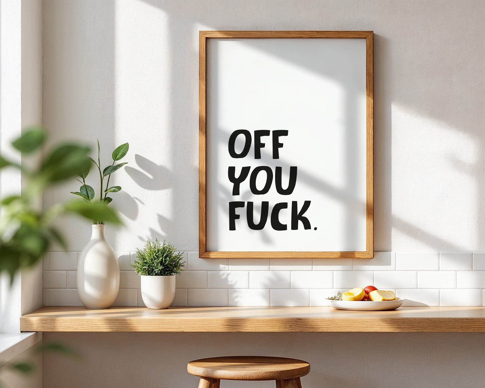 Framed artwork with a bold statement on a wall in a room with a wooden shelf and plants.