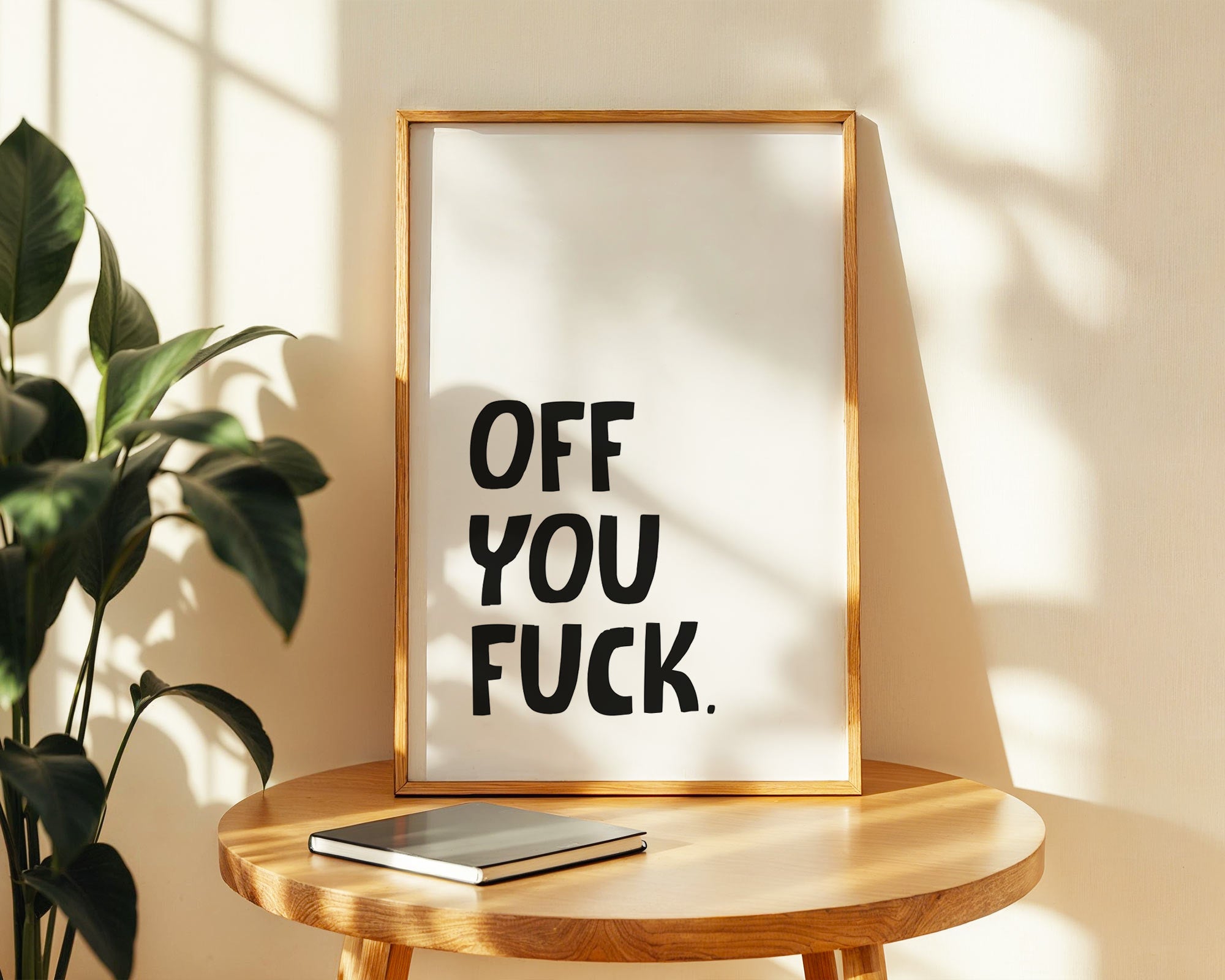 Framed artwork with text on a wooden table with a plant in the background