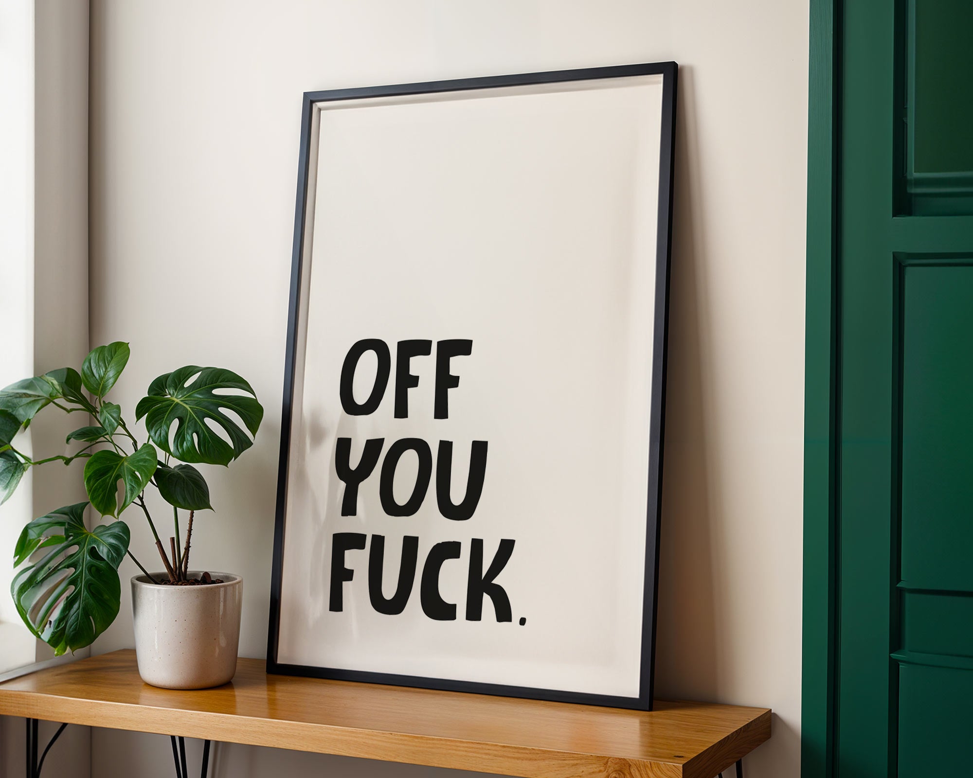 Framed artwork with text on a wall next to a plant