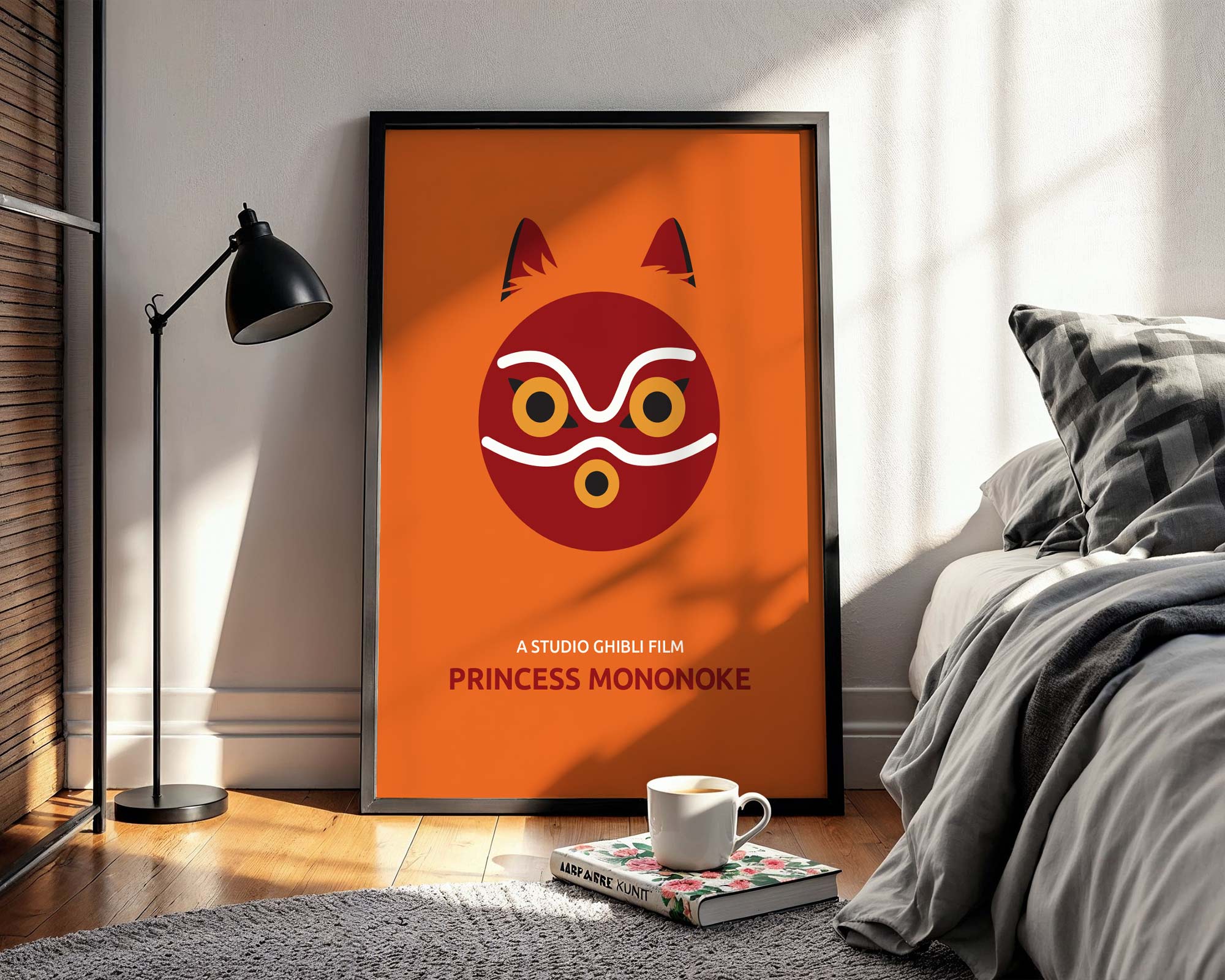 Framed 'Princess Mononoke' poster on a wall in a bedroom with a cup and book on a small table.