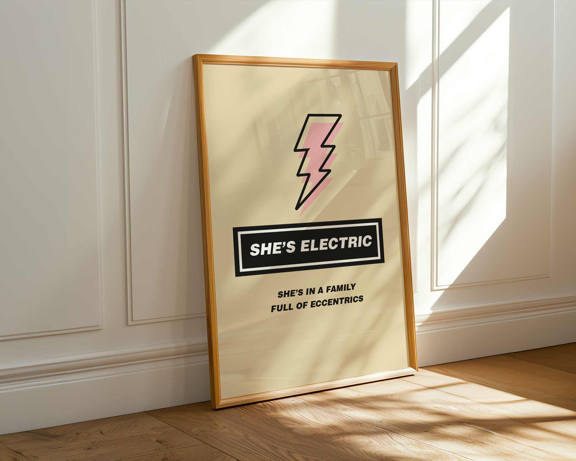 Framed artwork with a pink lightning bolt and text on a beige background, leaning against a white wall.