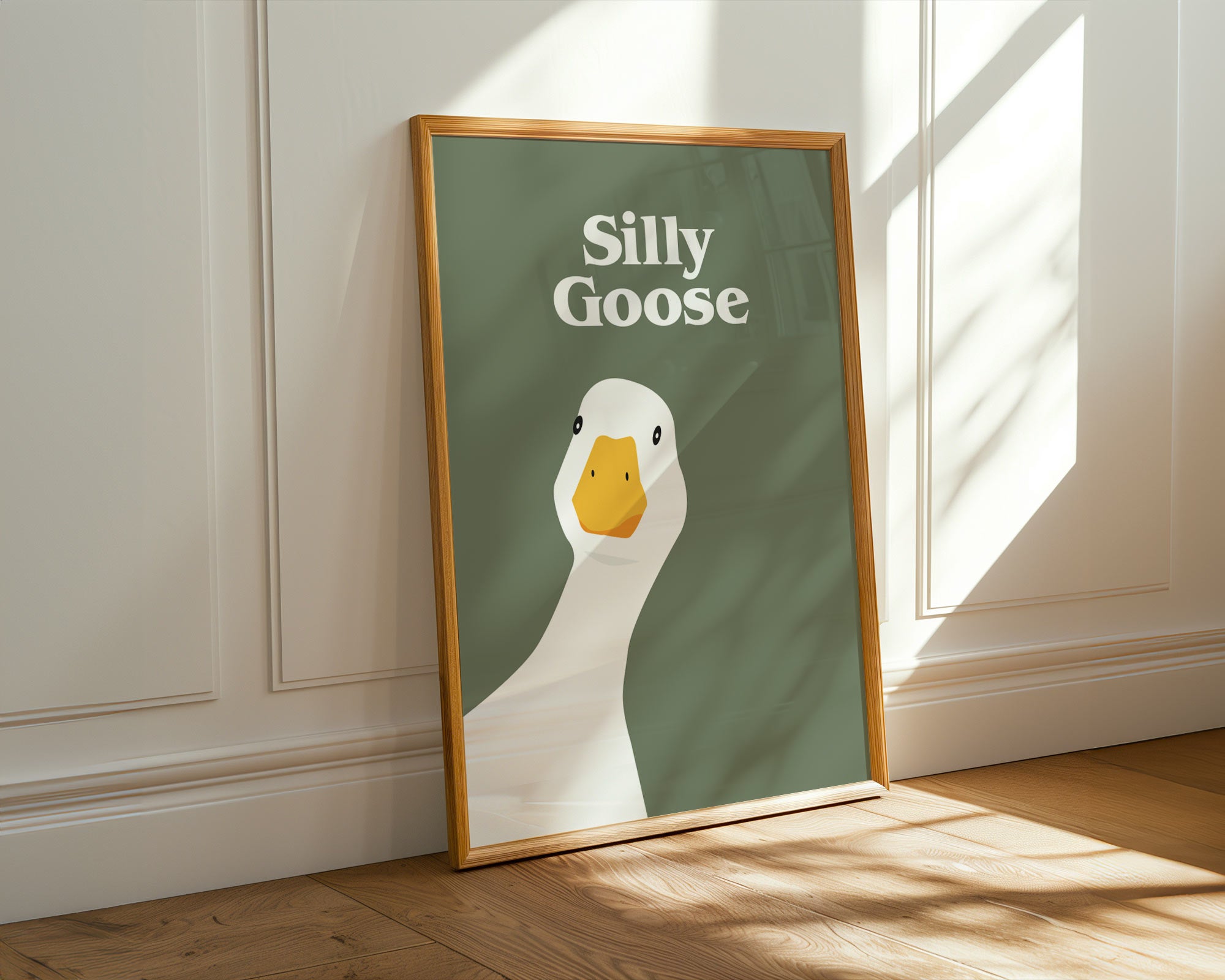 Framed poster with a duck illustration and text 'Silly Goose' on a green background, leaning against a wall.