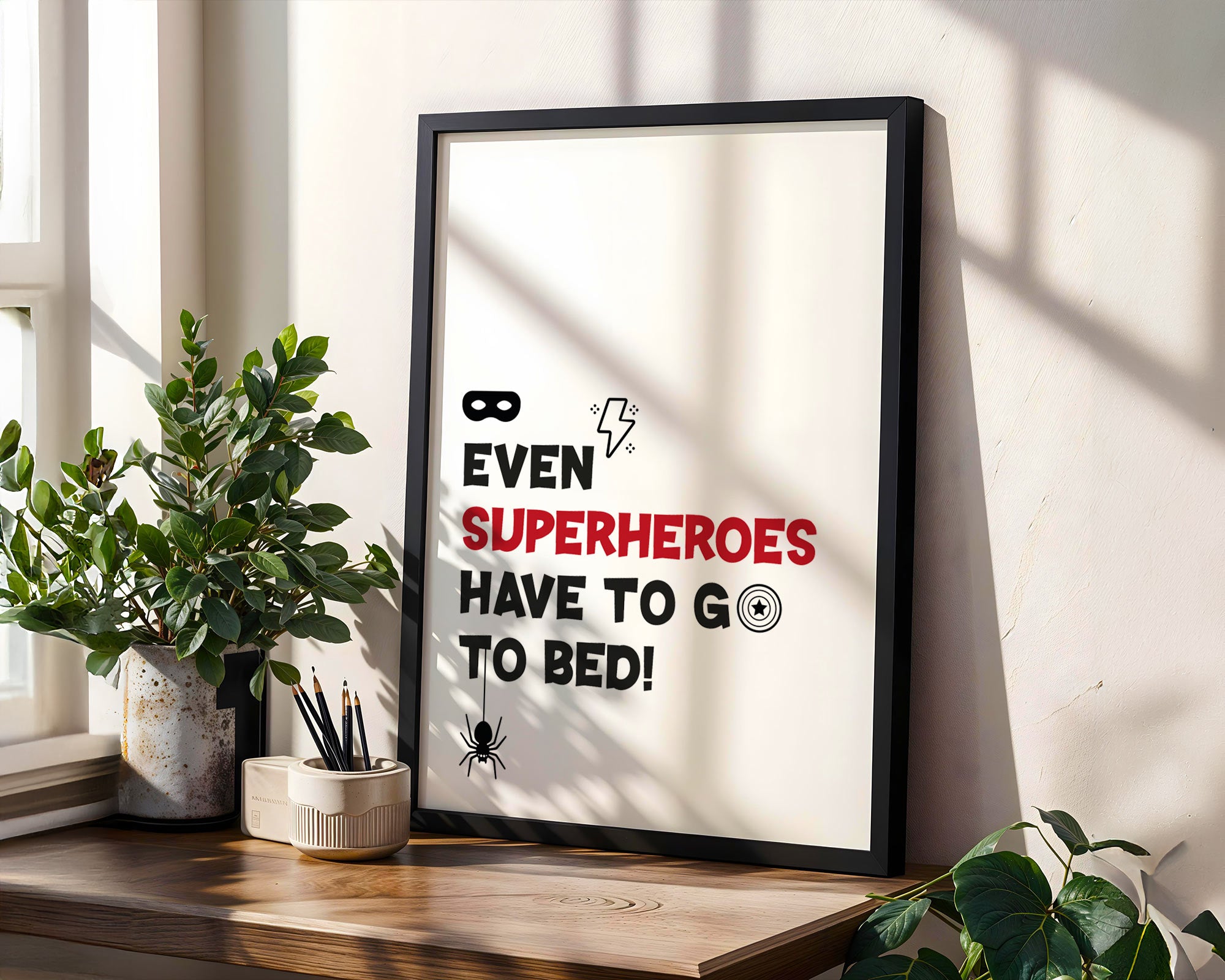 Framed poster with humorous superhero quote on a wall with plants and a window.