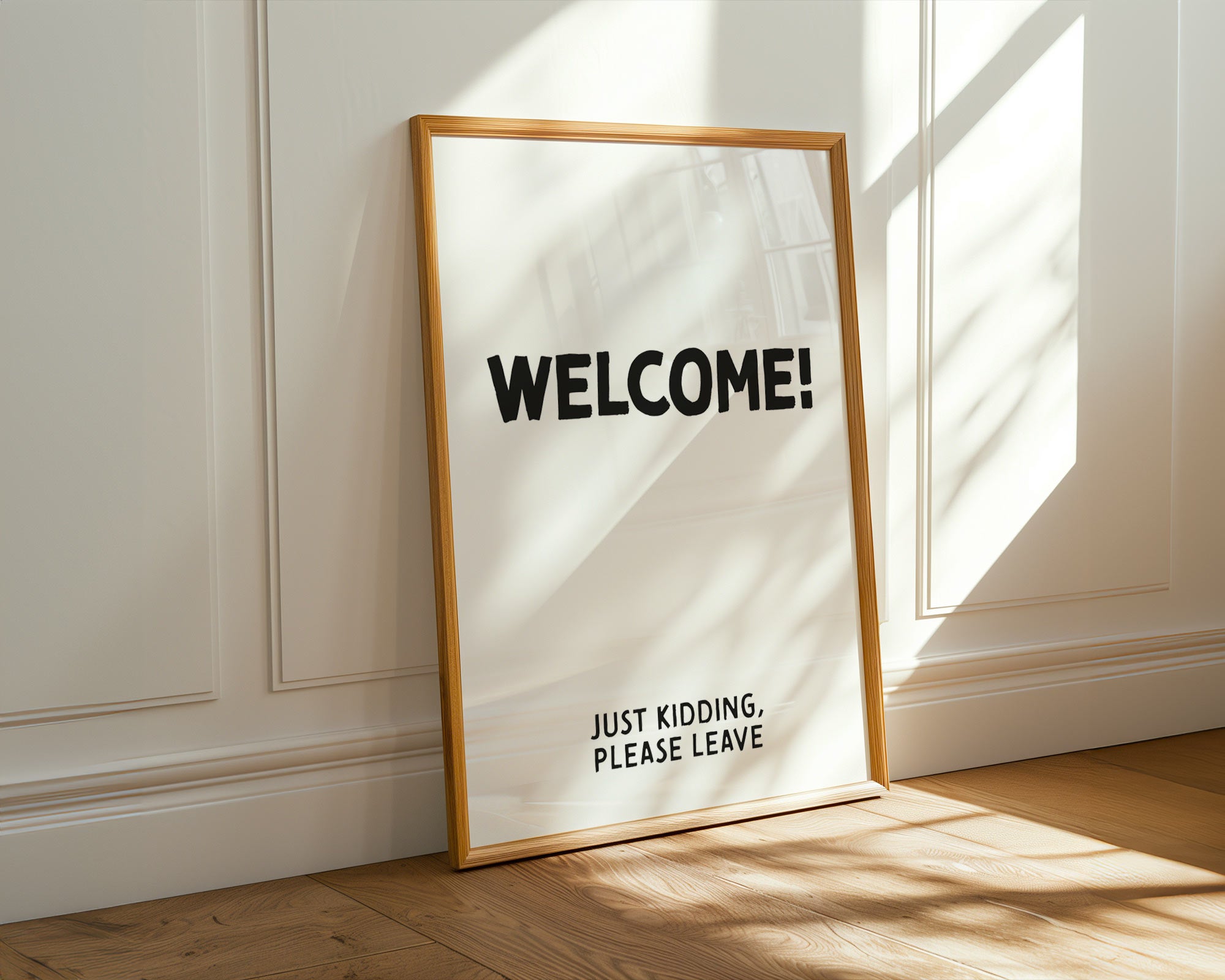 Framed poster with 'WELCOME! JUST KIDDING. PLEASE LEAVE' text on a white wall.